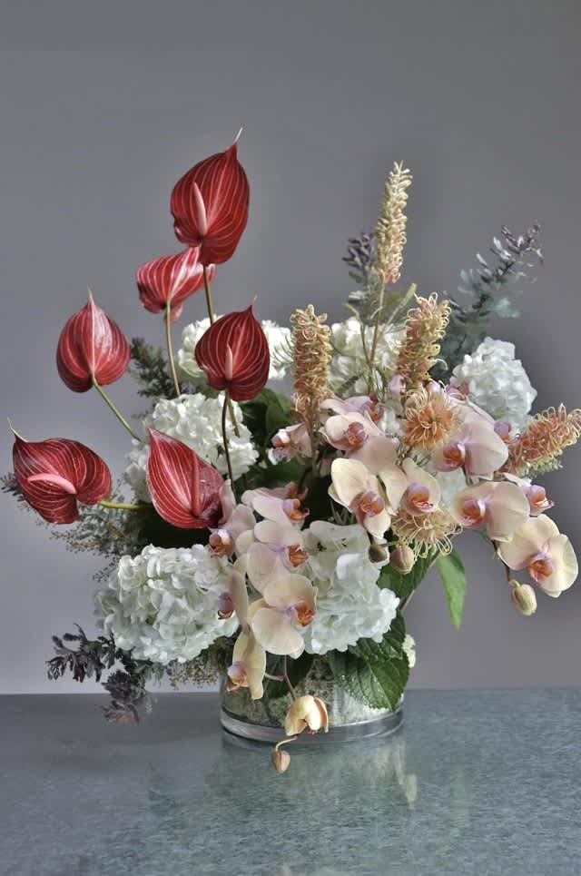 Mixed floral arrangement with red anthuriums, pale orchids, and white hydrangeas in a glass vase