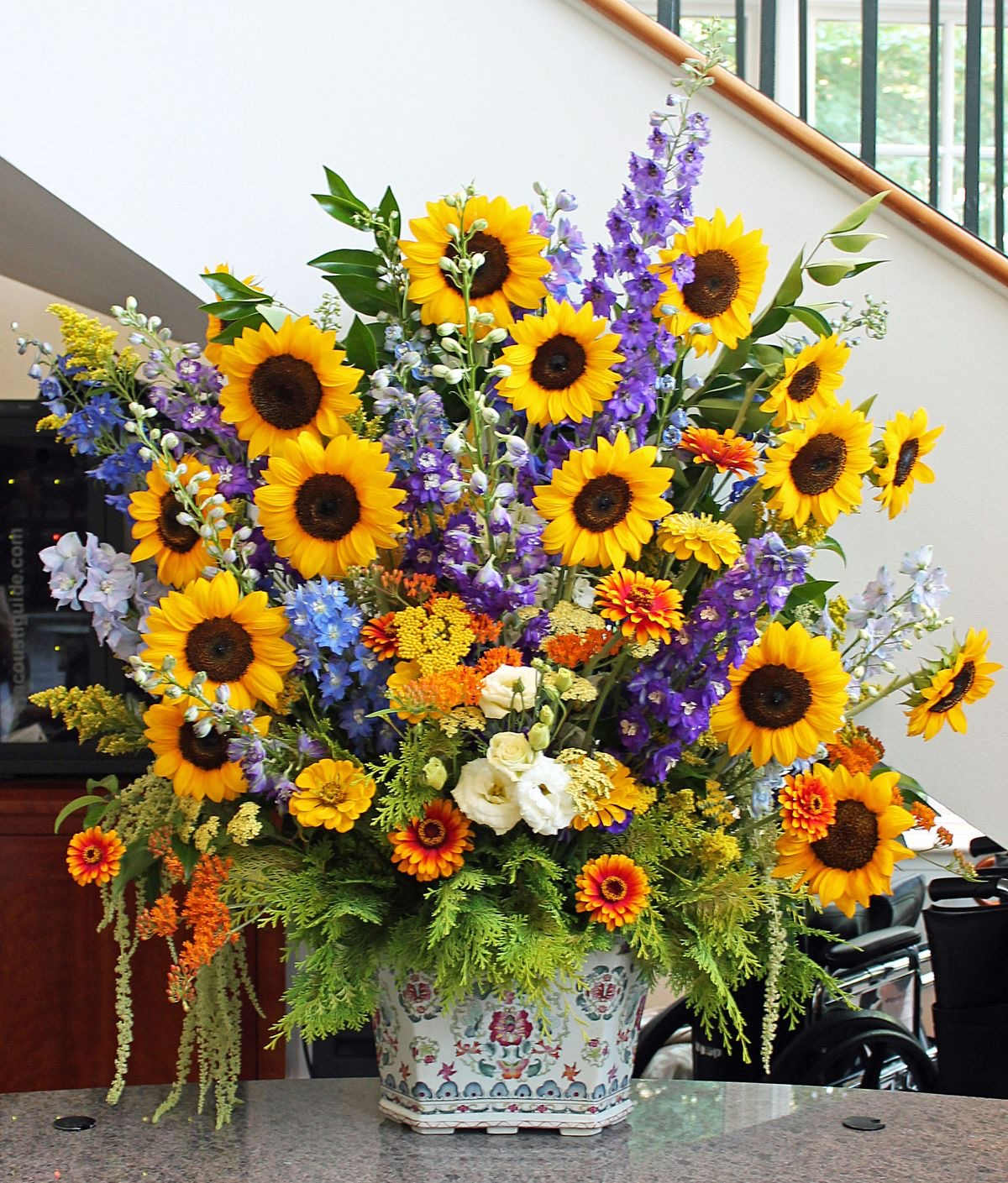 Large mixed bouquet with sunflowers, purple spikes, and a patterned ceramic vase