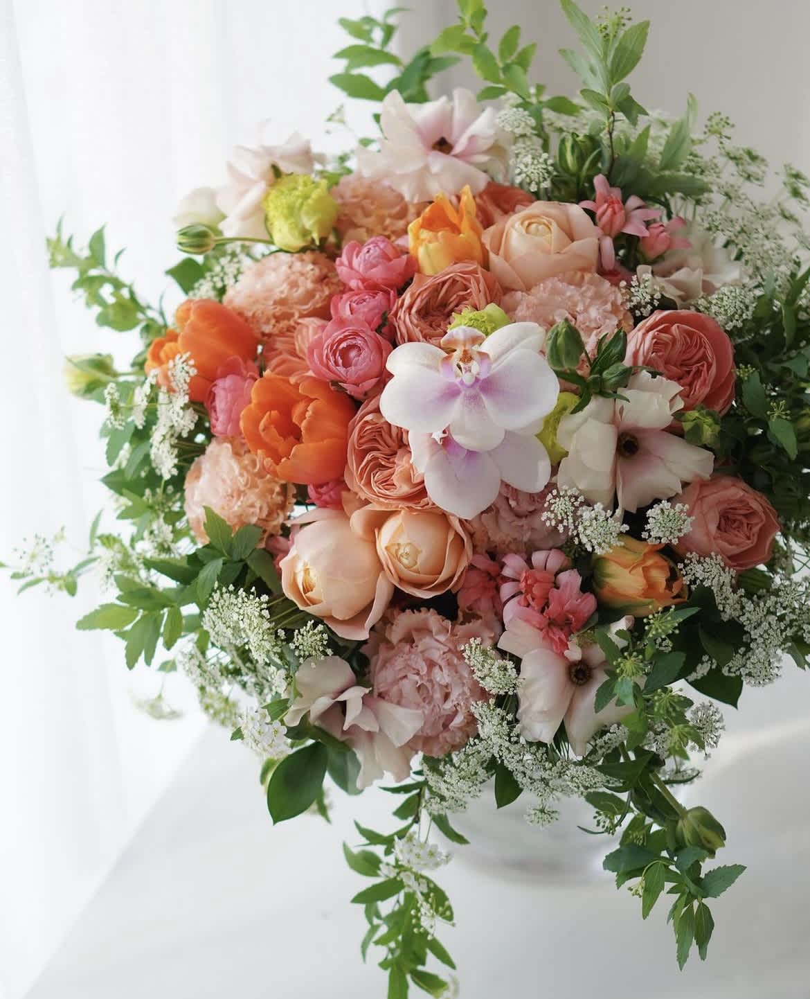 Round bouquet of peach, pink, and white flowers with greenery
