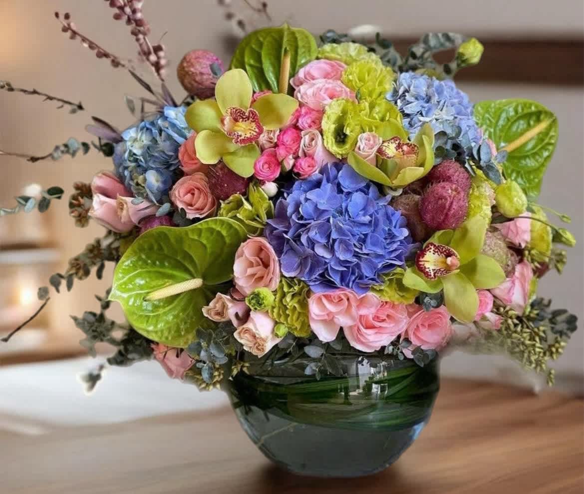 Colorful bouquet in a green glass vase with hydrangeas, roses, and orchids