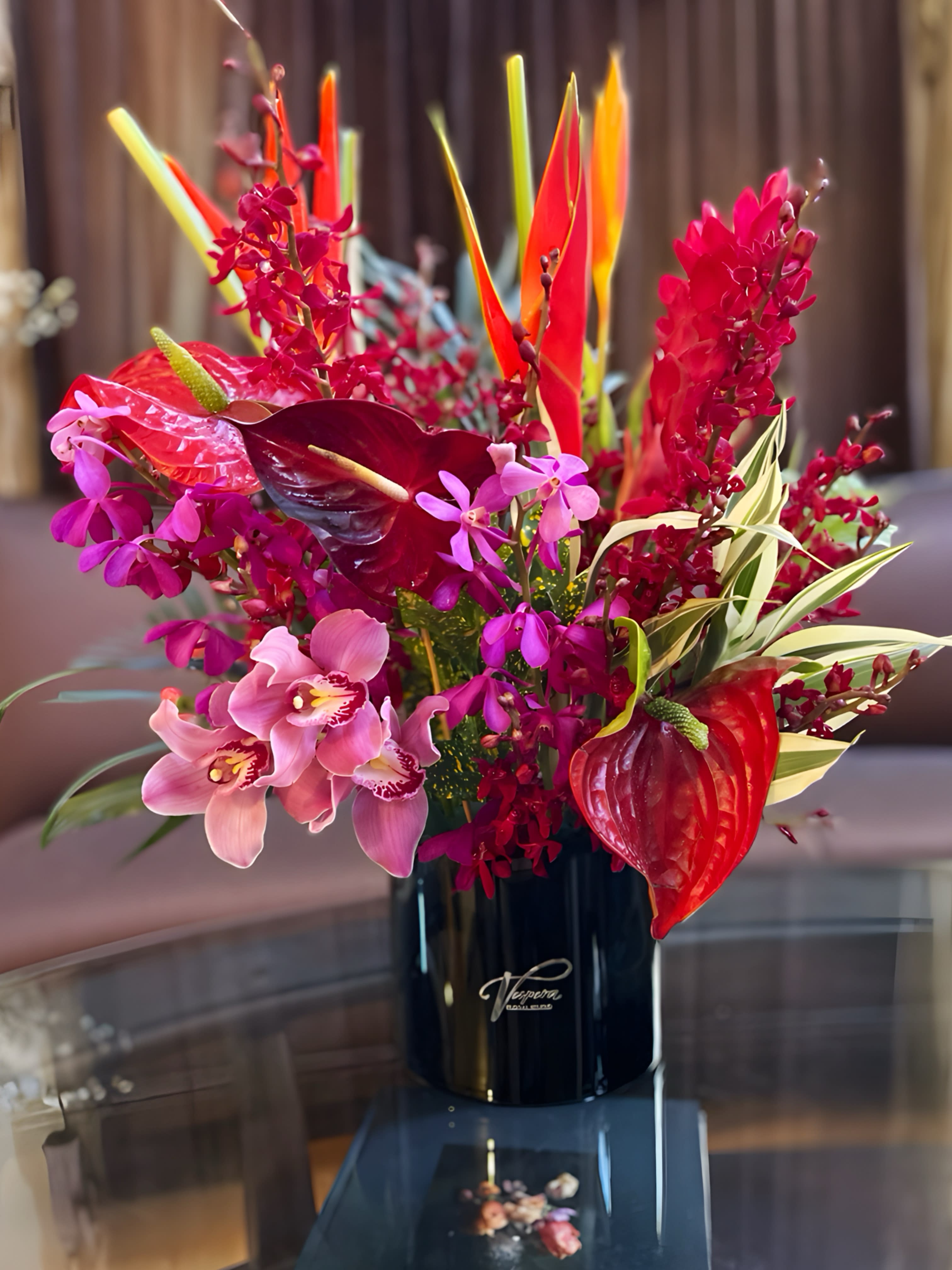 Tropical flower arrangement in a black vase with pink and red blooms