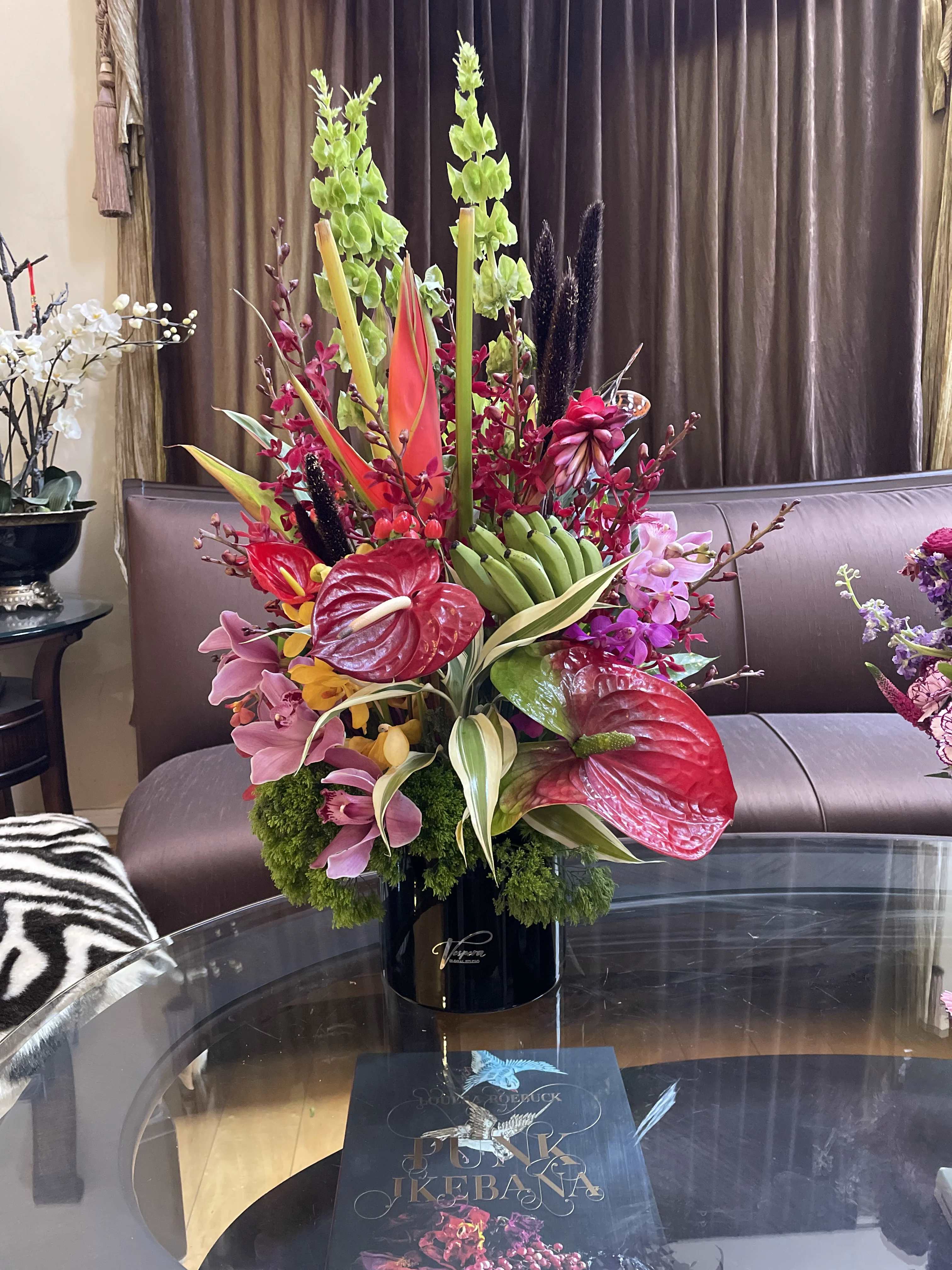 Tall tropical flower arrangement in a black vase with red anthuriums and pink orchids