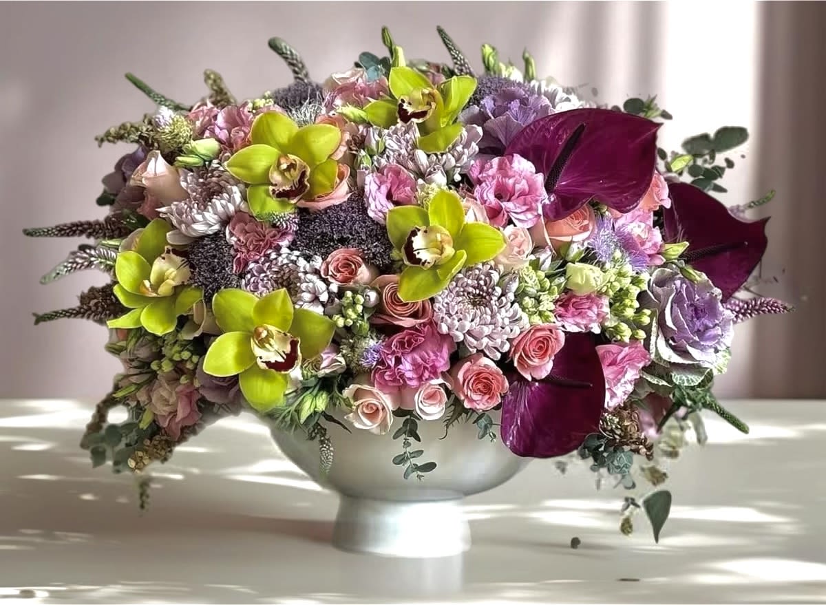 Mixed pink and purple floral arrangement in a white pedestal bowl