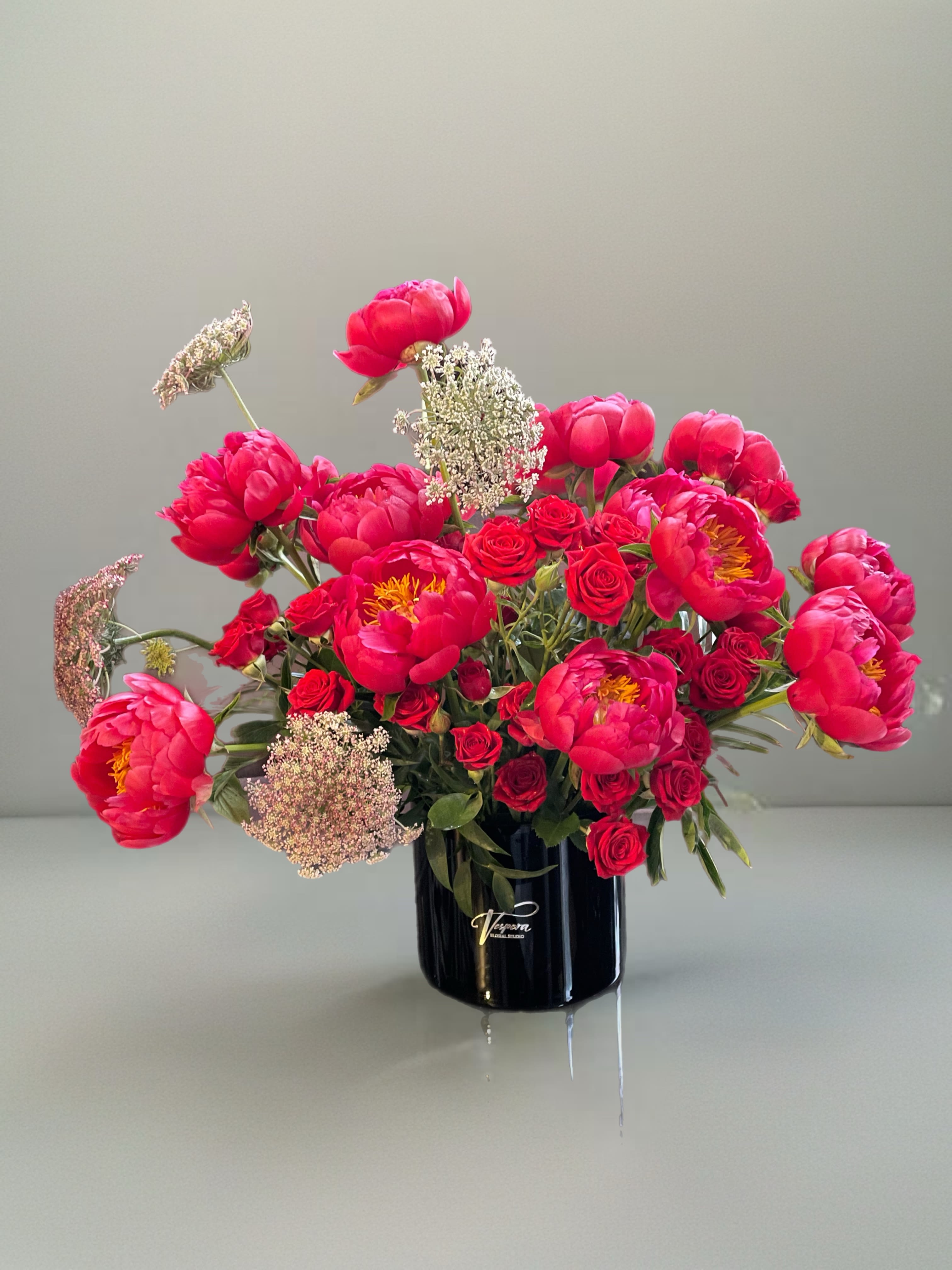 Pink peonies and red roses arranged in a black vase