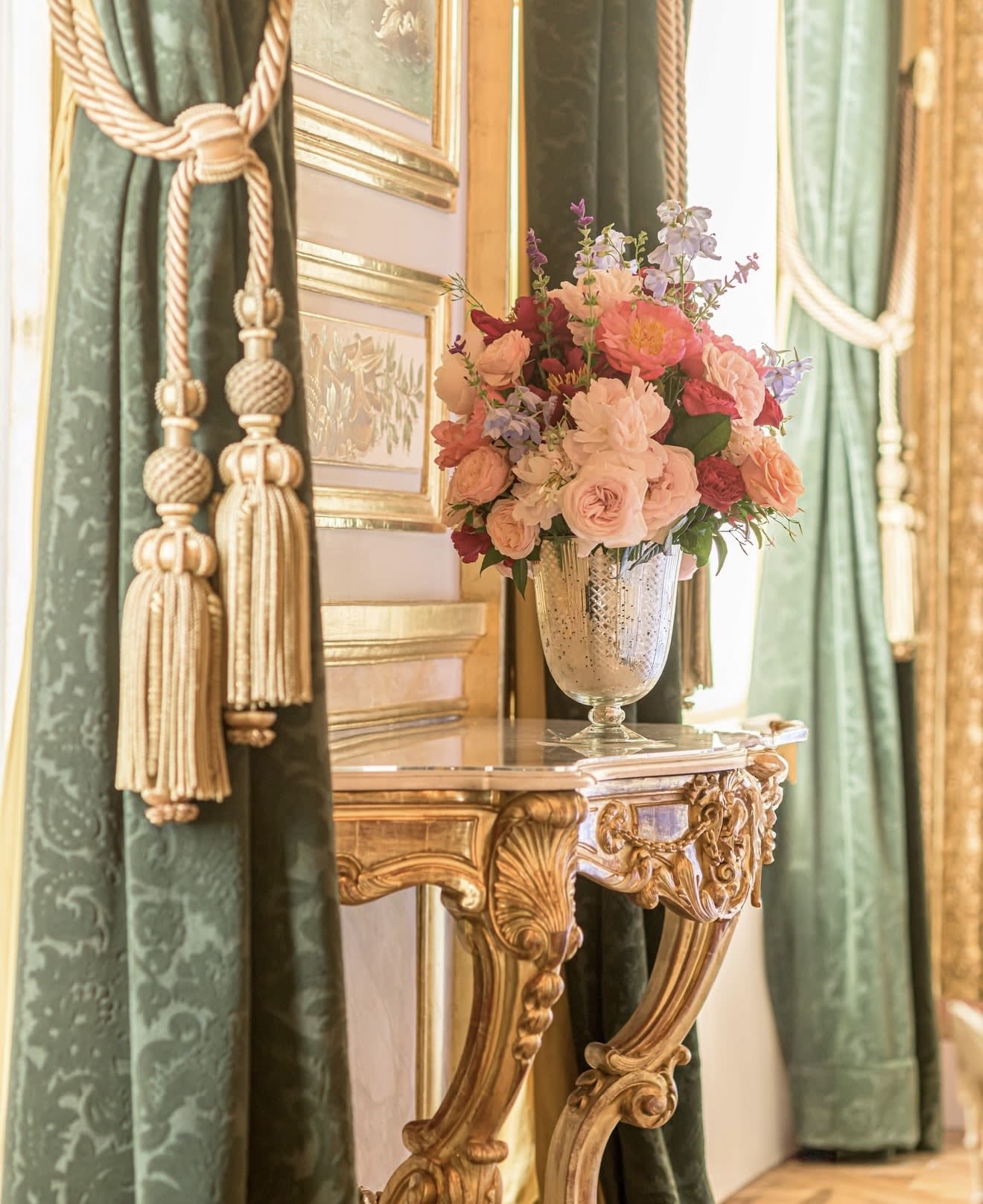 Pink and peach flower arrangement in a silver vase on an ornate table