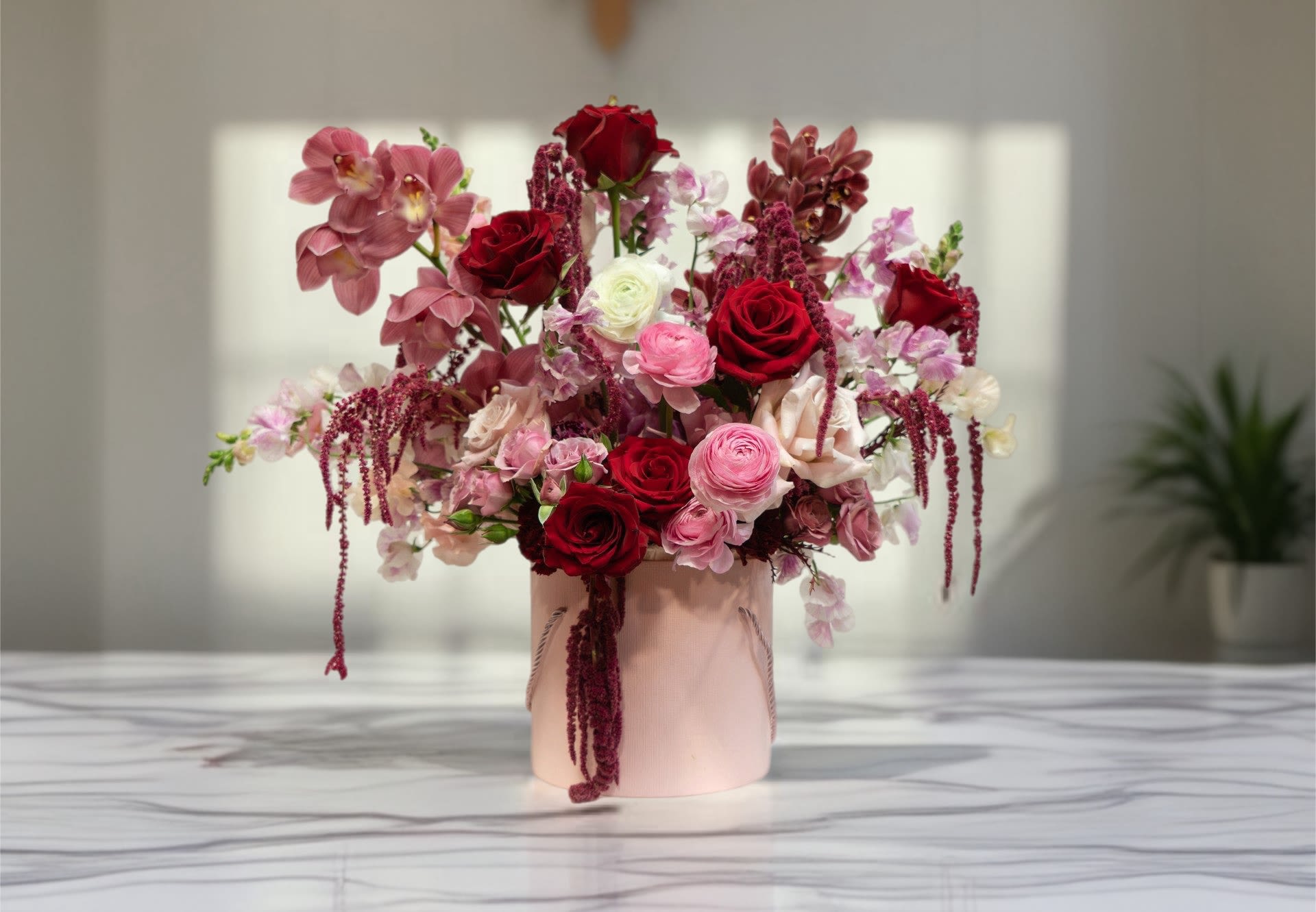 Pink and red floral arrangement in a blush vase