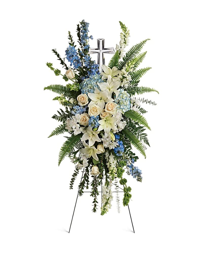 Eternal Grace Spray - Celebrate the eternal grace of a life well lived with this dramatic spray of peaceful white and blue blooms, crowned with a large crystal cross keepsake. This serene spray includes blue hydrangea,crème roses, white asiatic lilies, white alstroemeria, bells of Ireland, blue delphinium, white snapdragons, myrtle, sword fern, leatherleaf fern, spiral eucalyptus, and variegated pittorsporum. Delivered on a wire easel with a Crystal Cross Keepsake.