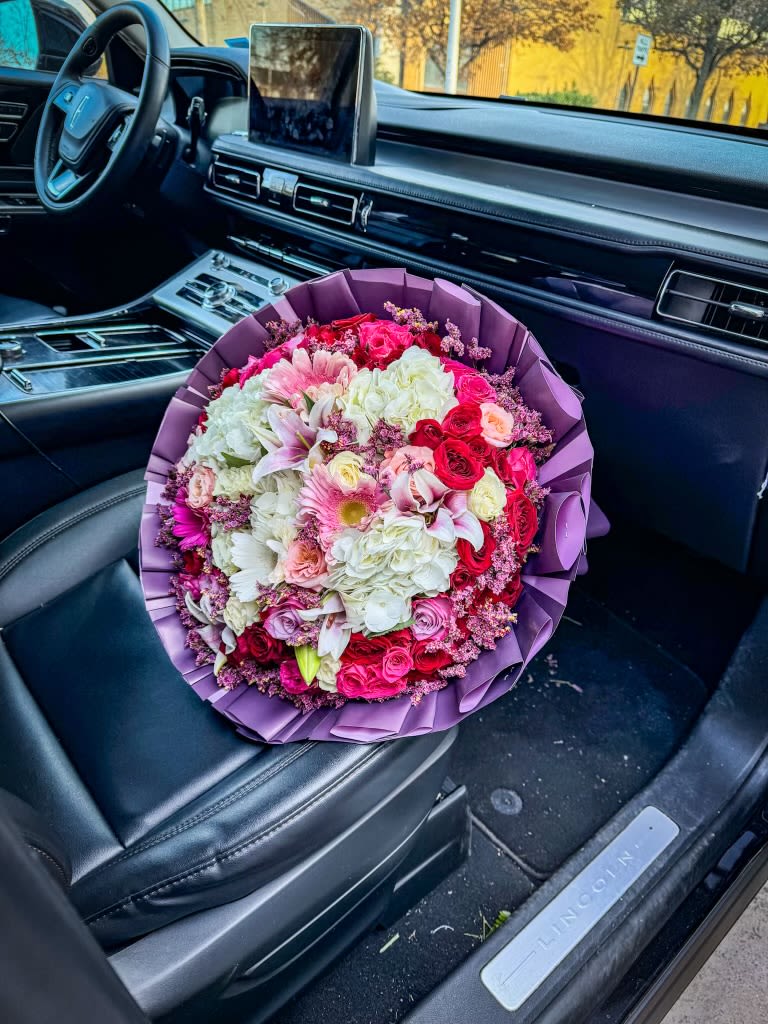 Large bouquet of pink, white, and red flowers wrapped in purple paper