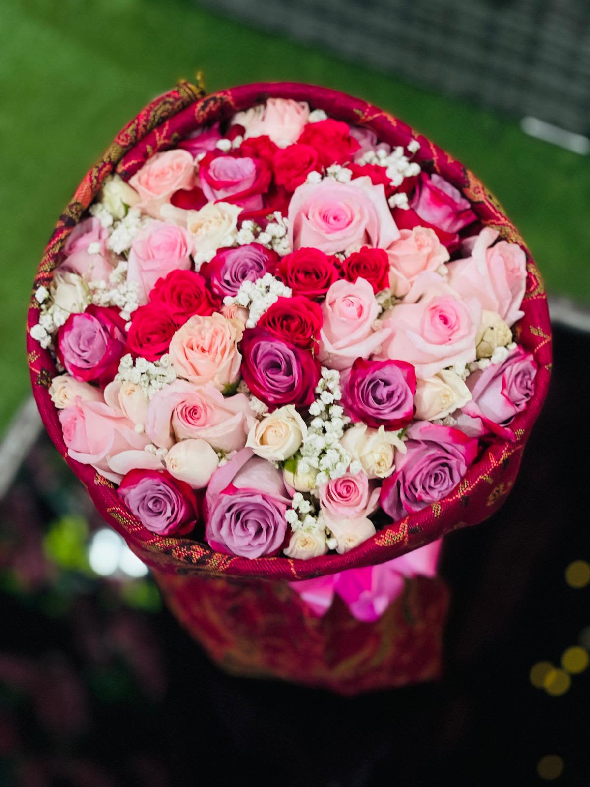 Round bouquet of pink, red, and lavender roses with white filler flowers