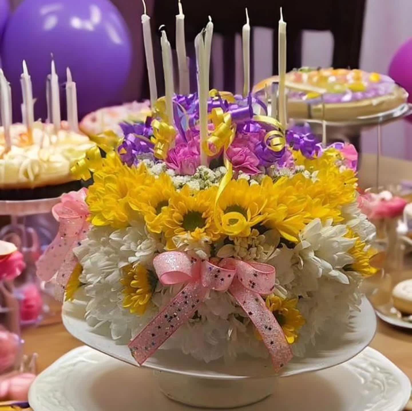 Round floral cake with candles and pink ribbon on a pedestal stand