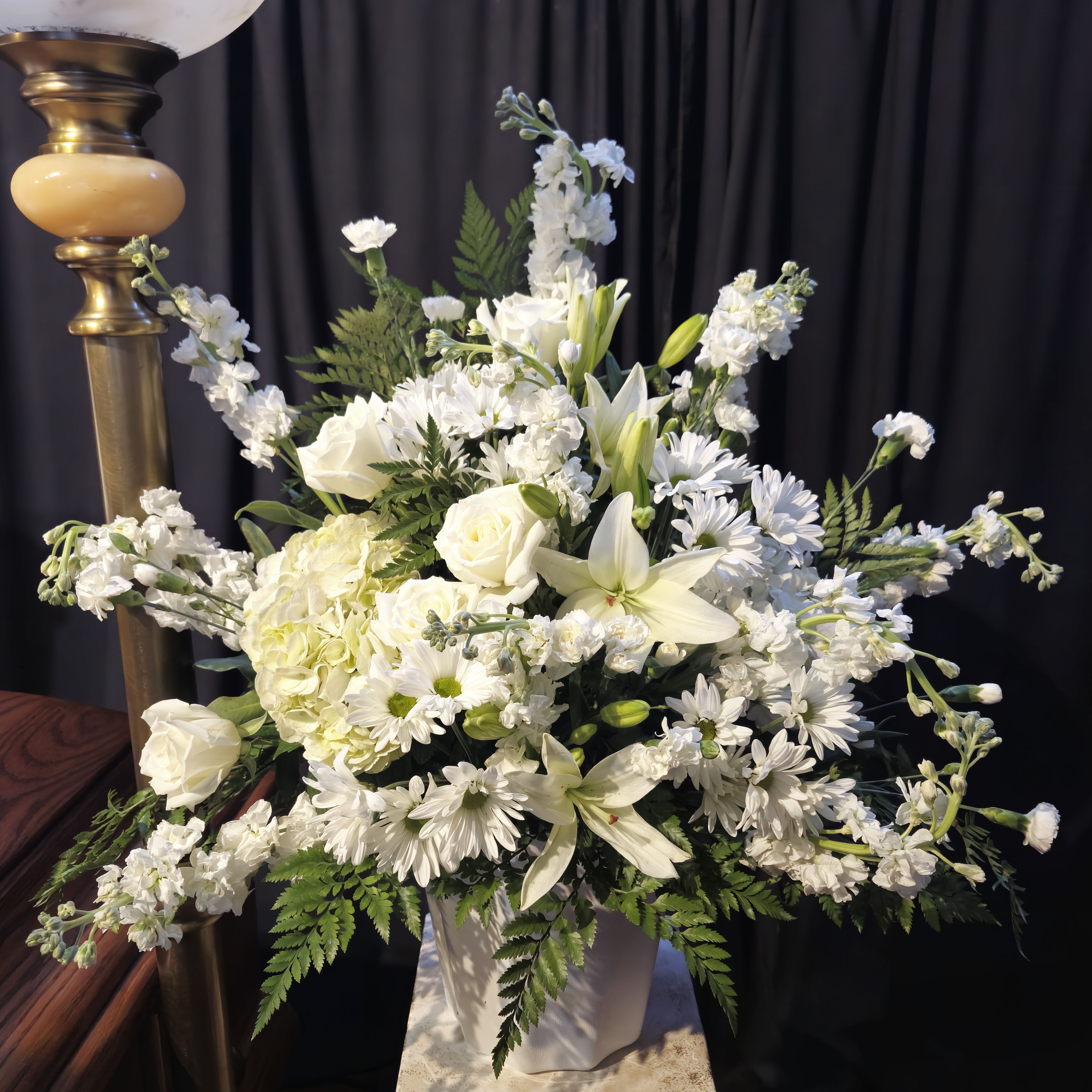 Eternal Peace Floral Tribute Basket - Honor the memory of a loved one with our “Eternal Peace Floral Tribute.” This elegant arrangement features pristine white roses and lilies, symbolizing purity, peace, and reverence. Accented with lush green foliage, this tribute exudes a serene and comforting presence, making it a perfect choice for funerals and memorial services. Each flower is carefully selected and arranged to convey heartfelt condolences and support during difficult times.  Features:  White Roses and Lilies: Representing purity and peace.  Green Foliage Accents: Adding a touch of natural elegance.  Thoughtful Design: Crafted to provide comfort and convey sympathy.  Versatile Display: Suitable for various memorial settings.  Let this beautiful arrangement serve as a gentle reminder of the enduring love and cherished memories shared with the departed.