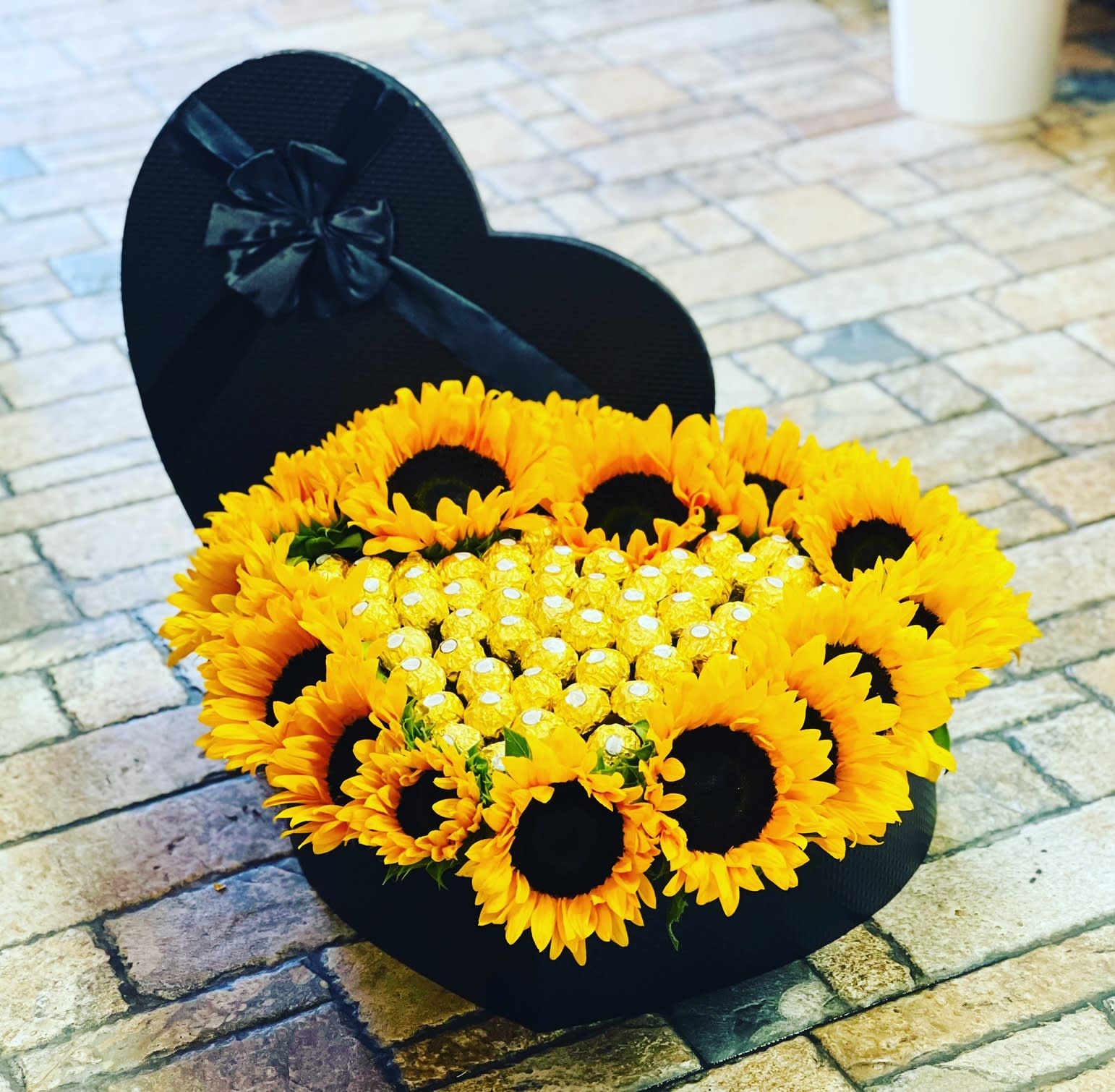 Heart-shaped black box filled with sunflowers and gold chocolates