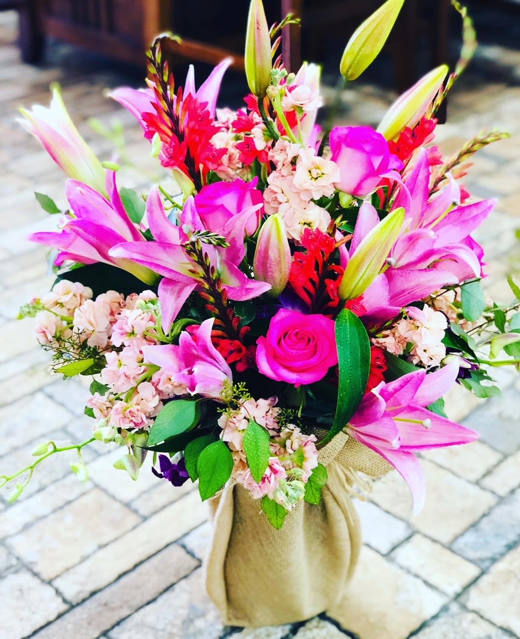 Pink lilies and roses arranged in a burlap-wrapped bouquet