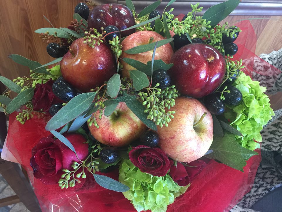 Apple Orchard Wrapped Bouquet  - Bright red apples and glossy dark grapes tucked among red roses and lime-green hydrangeas make this Apple Orchard Wrapped Bouquet a joyful, unexpected gift for an autumn celebration, birthday, or a just-because surprise. The mix of red, green, orange and mixed color accents gives the bouquet a lively, slightly rustic look that reads seasonal for Thanksgiving yet feels fresh year-round. Wrapped in bright red tulle, it arrives ready to present-she'll feel genuinely delighted by the playful combination of fruit and flowers.  This arrangement pairs the soft round blooms of hydrangeas with classic red roses, eucalyptus-style foliage, and small green buds for added texture and a garden-fresh scent profile. Real red apples and clusters of dark grapes are nestled throughout, creating a generous, edible twist on a traditional flower arrangement. The gathered bouquet sits comfortably in a hand-tied presentation and is finished with red tulle for a festive, gift-ready touch.  Perfect for saying thank you, cheering someone on, or sending get well wishes to the person you're thinking of, this bouquet works for Best Friends Day, Admin Professionals' Week, Grandparent's Day, and other celebrations. For local shoppers in Killeen, TX, it's an easy choice when you want a memorable, multifunctional gift that delights both the eyes and the palate-order soon for same-day pickup or delivery when available.