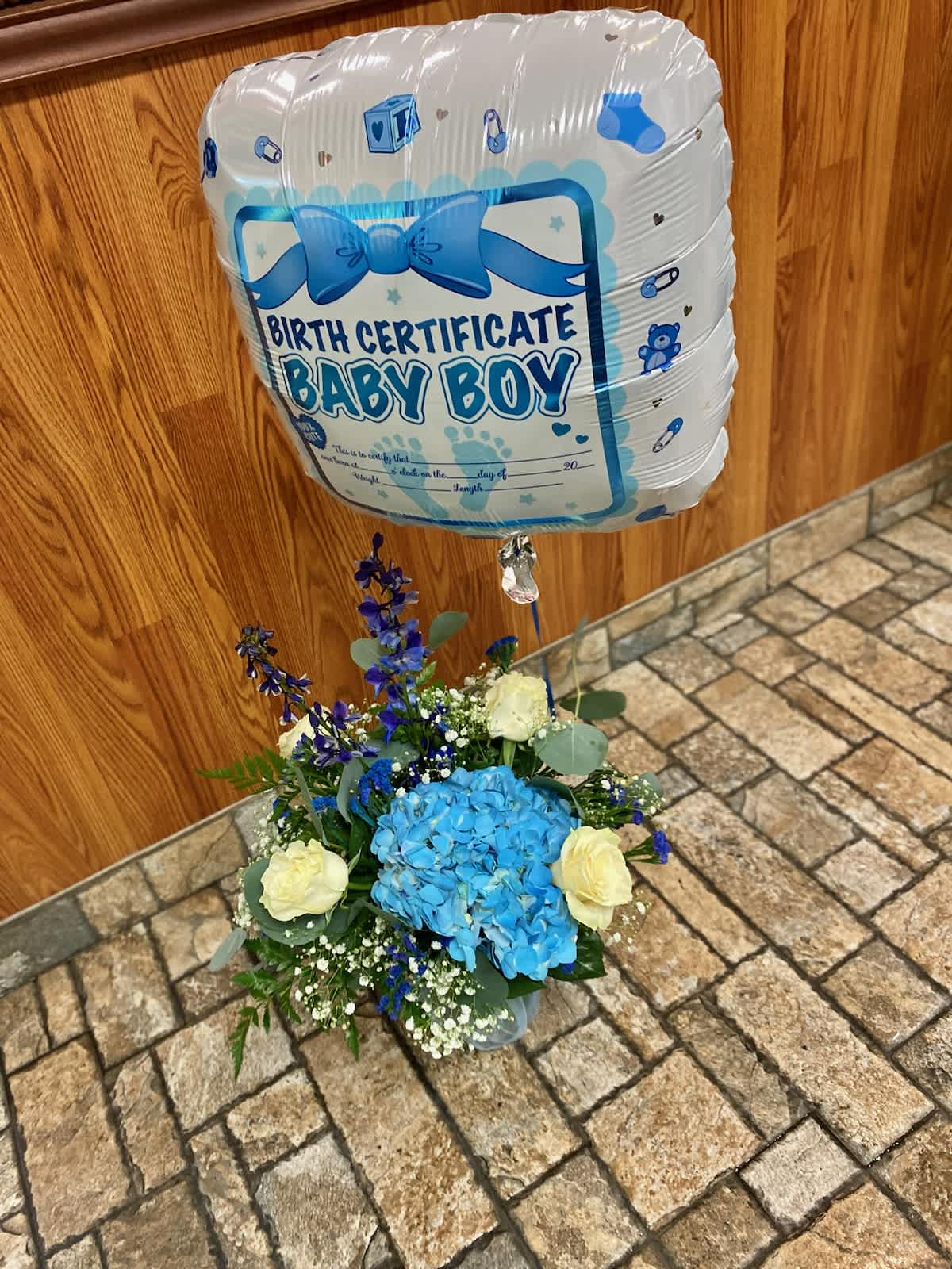 Blue baby boy balloon above a blue and white flower arrangement
