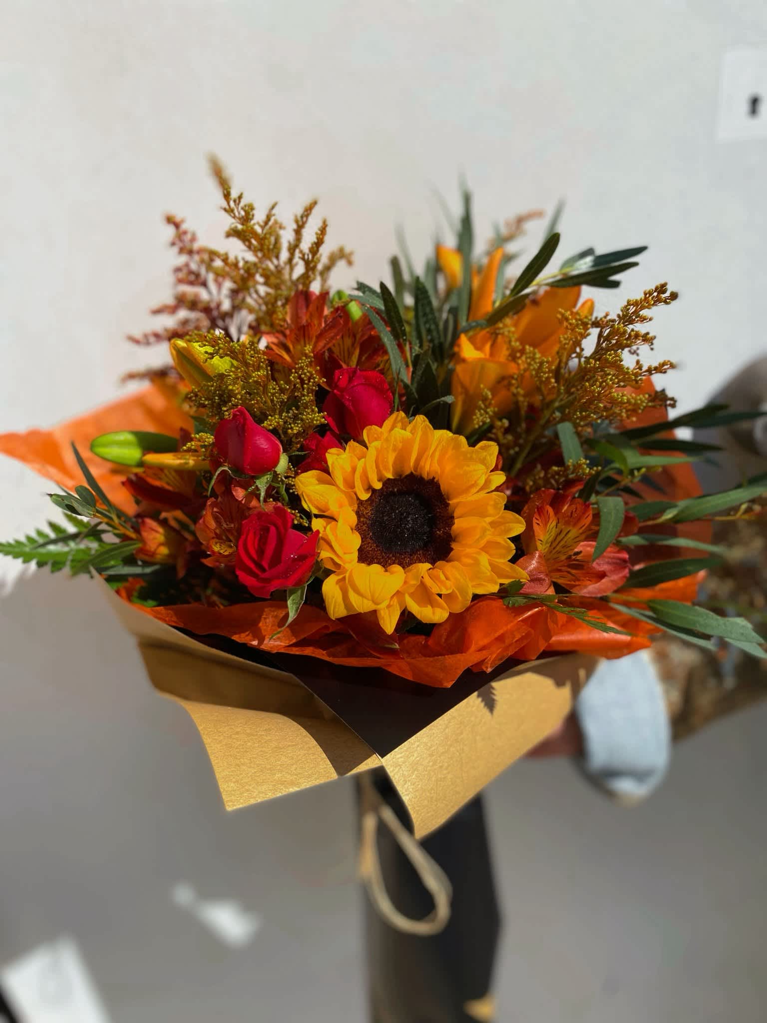 Bouquet of sunflowers and red roses wrapped in orange and gold paper