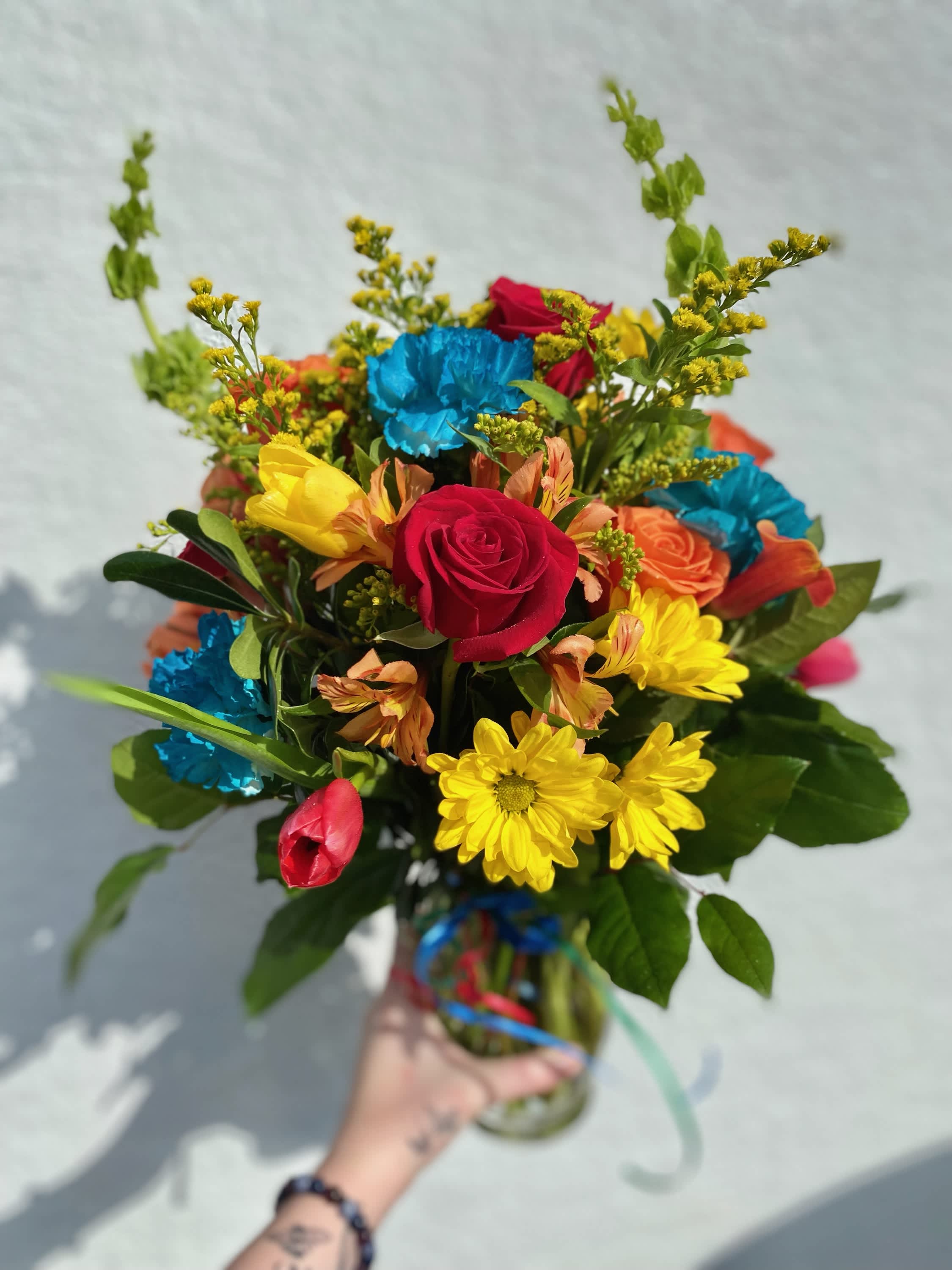 Handheld bouquet of mixed bright flowers in a glass vase
