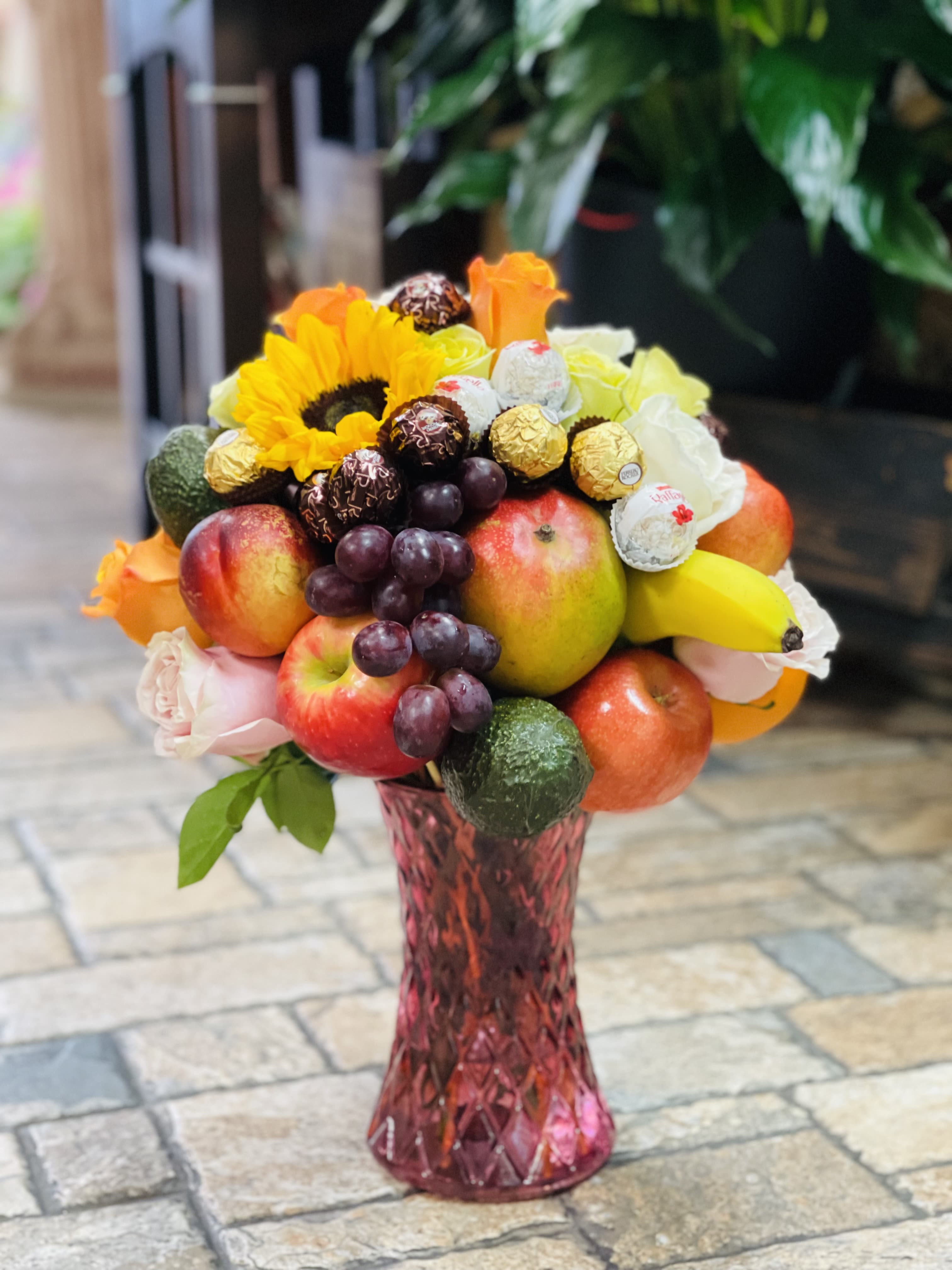 Fruit bouquet with sunflowers, roses, grapes, apples, bananas, and chocolates in a pink vase