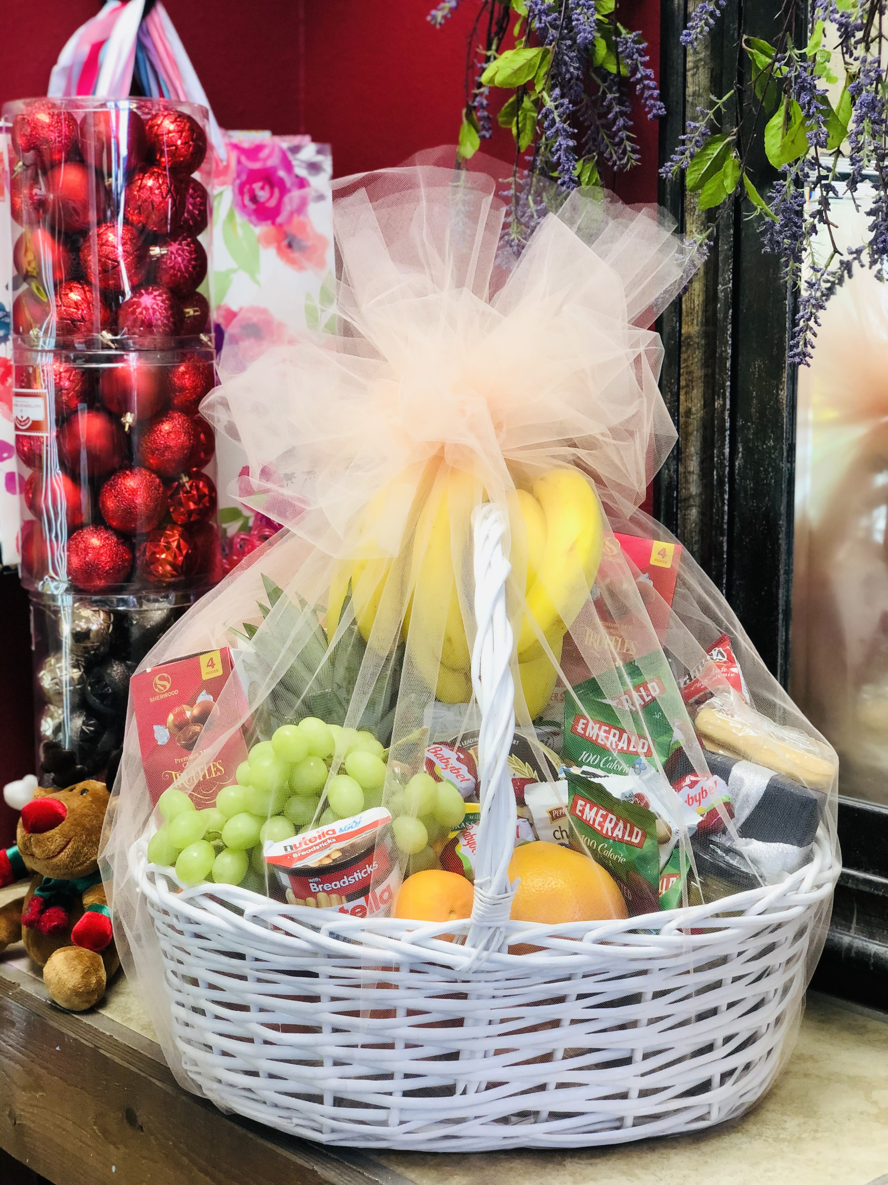 Fruit and snack gift basket in a white wicker basket with tulle wrap