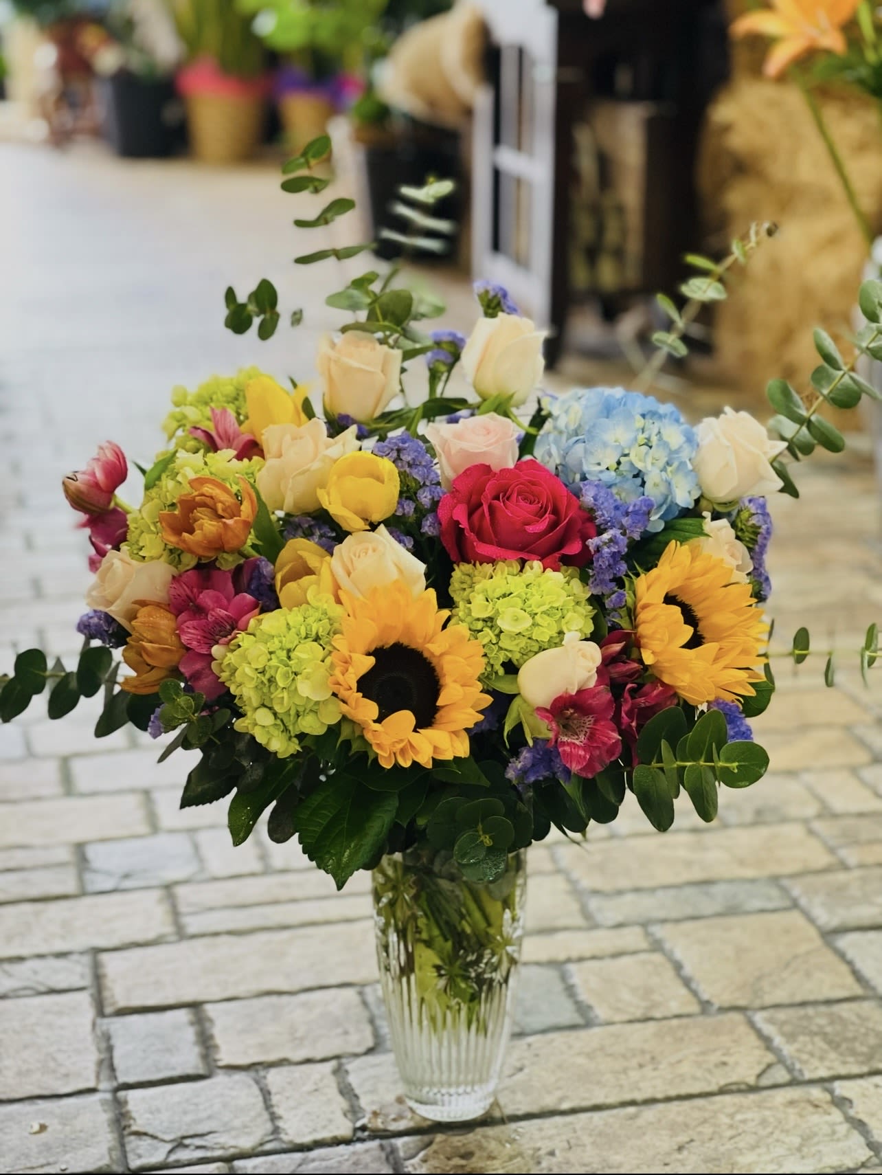 Mixed bouquet of sunflowers, roses, and hydrangeas in a clear glass vase