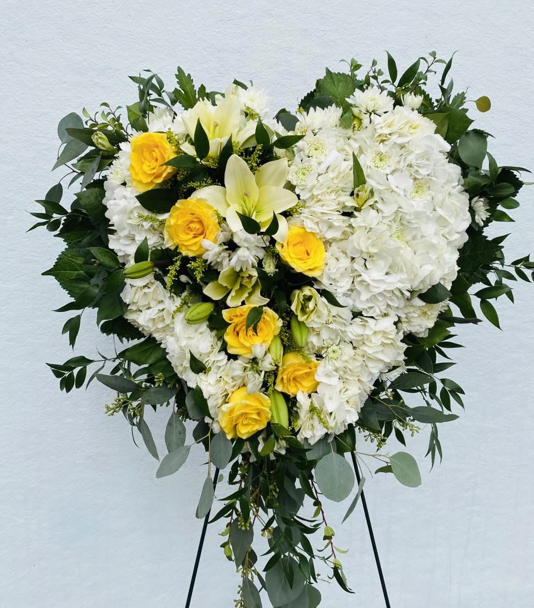 Heart-shaped white and yellow floral spray on a stand