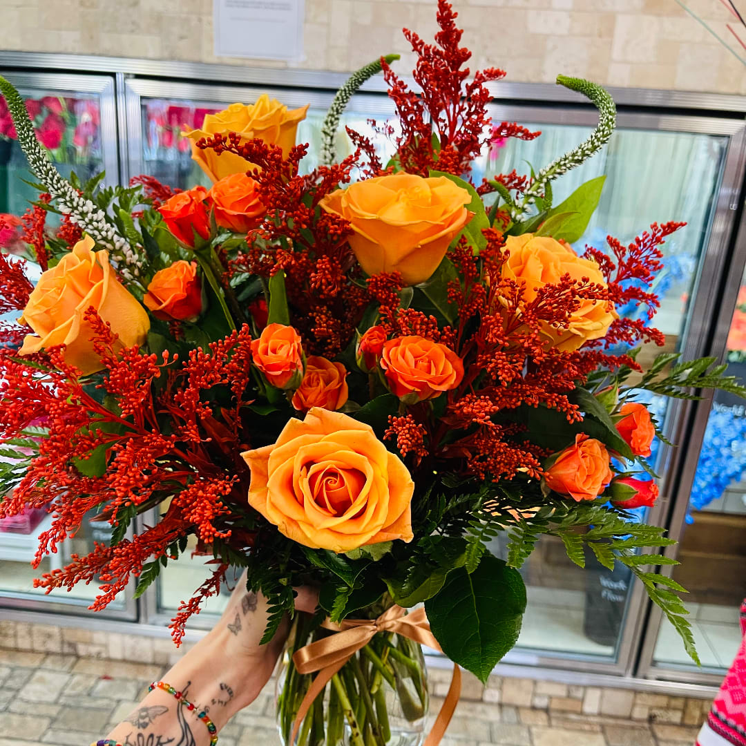 Bouquet of orange roses with red filler flowers in a glass vase