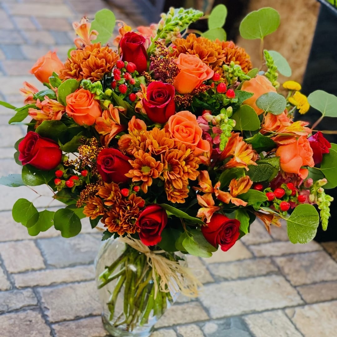 Bouquet of red and orange roses with orange chrysanthemums in a glass vase