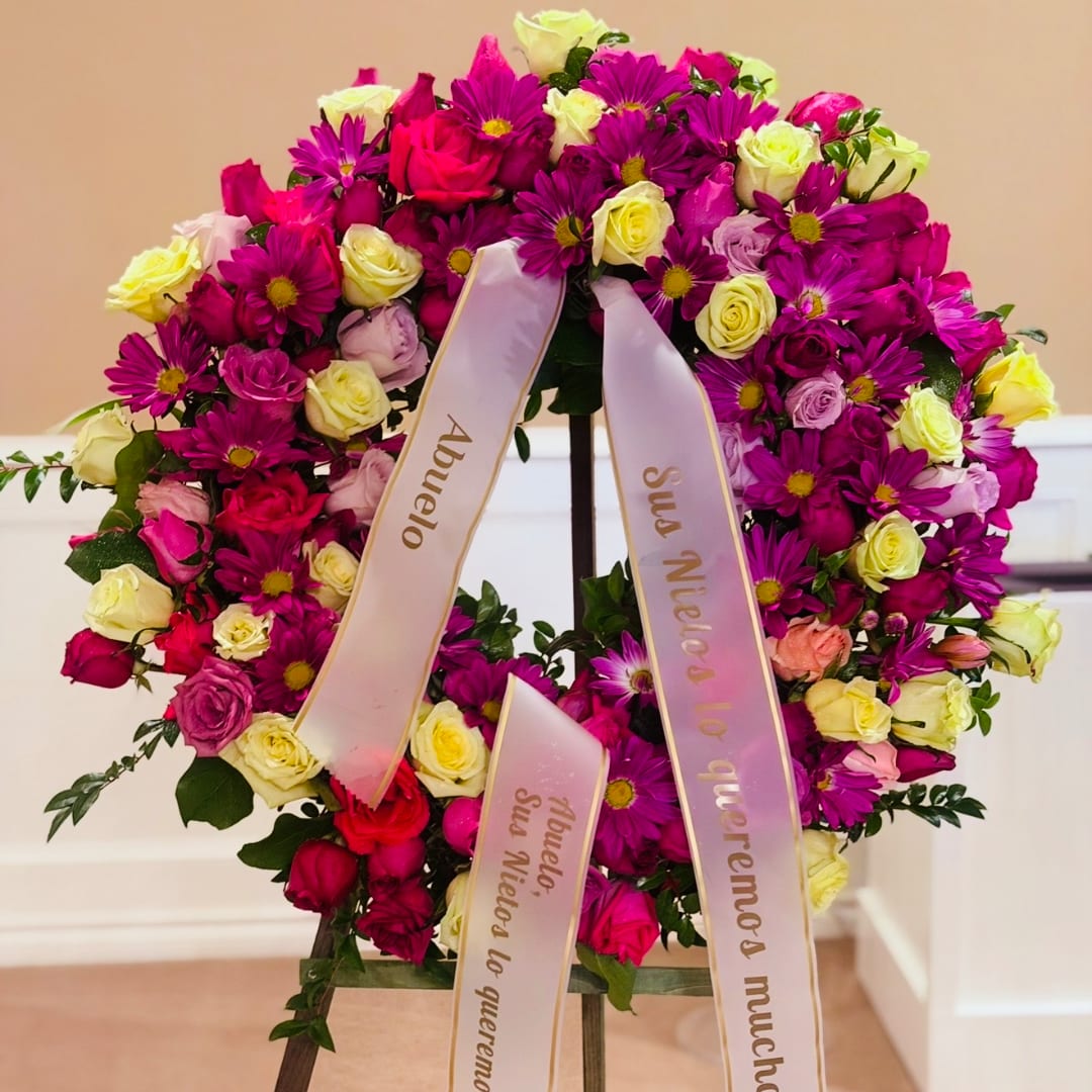 Large floral wreath of pink, purple, and cream roses with ribbon streamers
