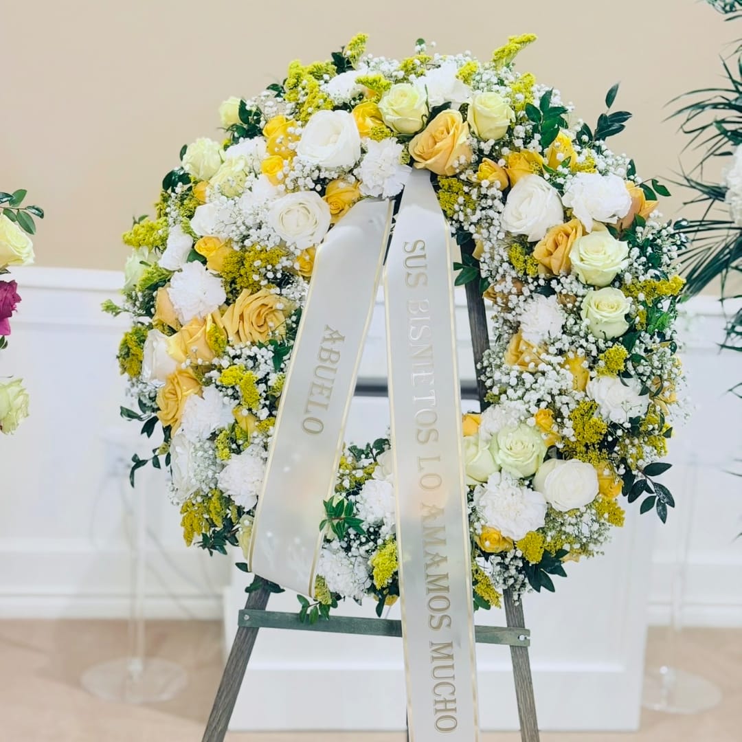 Yellow and white rose wreath on an easel with a memorial ribbon