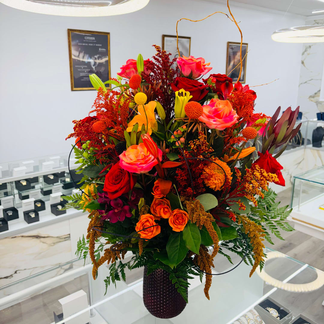 Large mixed bouquet of red, pink, and orange flowers in a dark vase