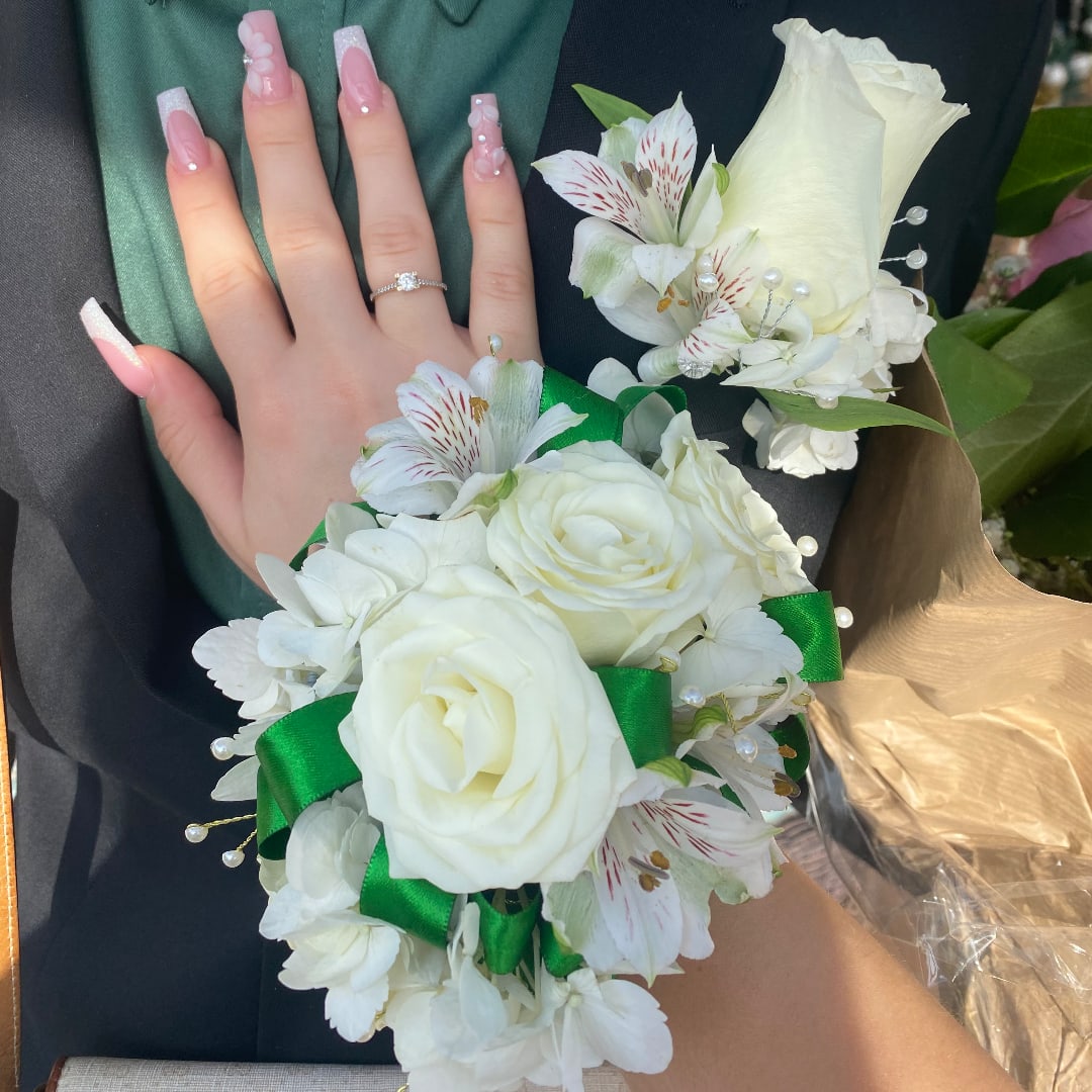 White rose corsage and boutonniere with green ribbon and pearl accents