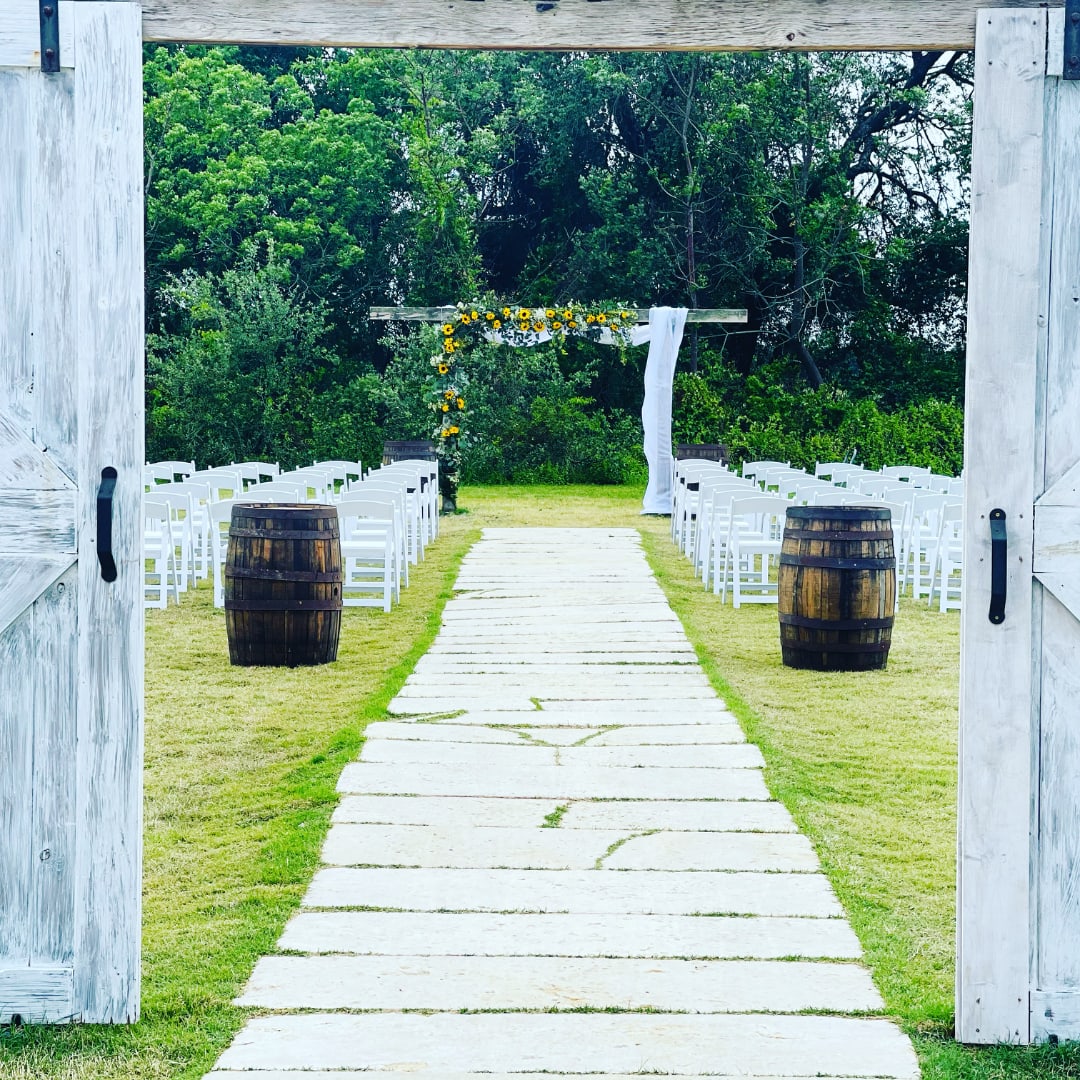 Outdoor wedding aisle with white chairs and a floral arch