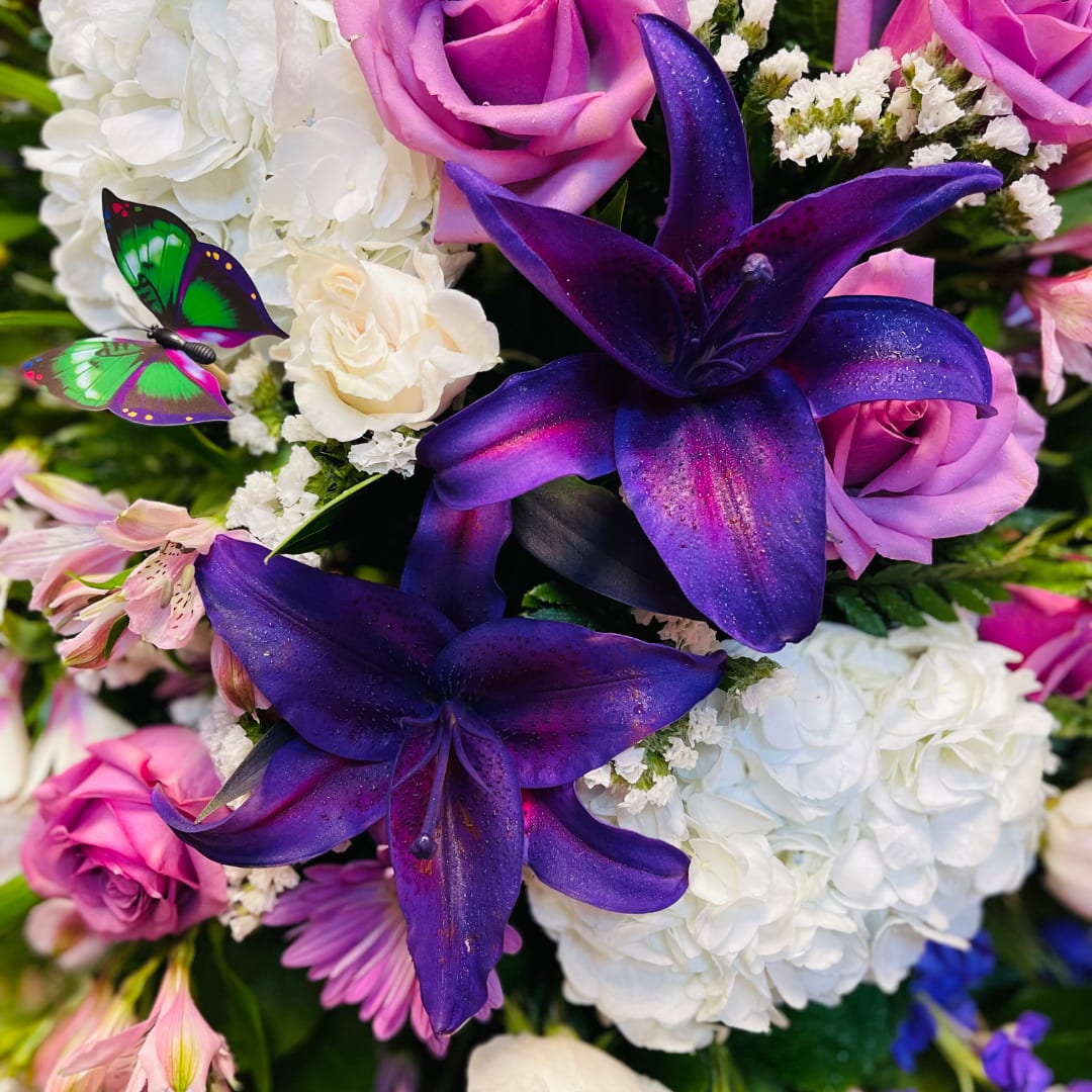 Purple lilies and pink roses with white hydrangeas and a butterfly accent