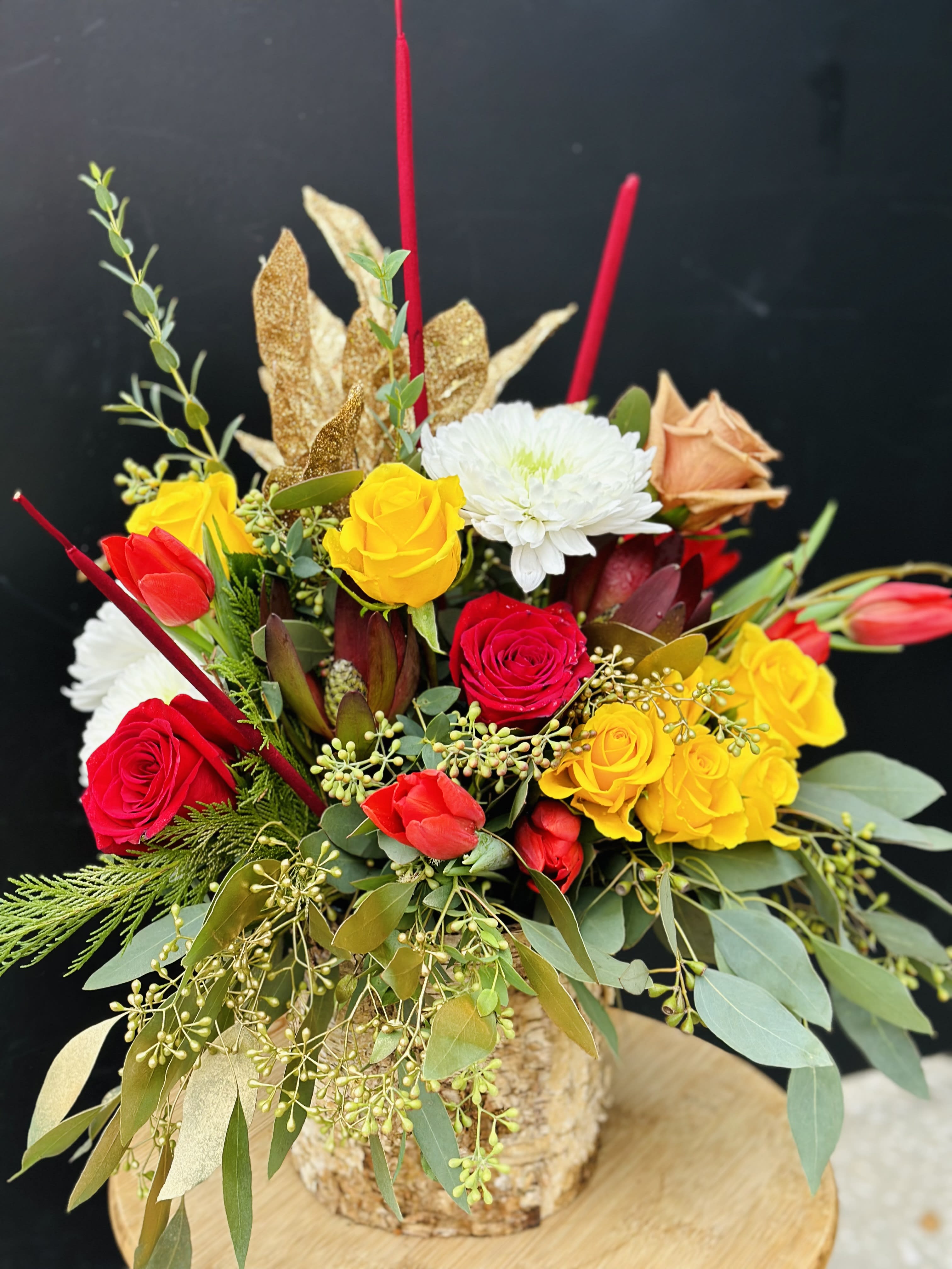 Mixed bouquet of red, yellow, and white flowers in a rustic container