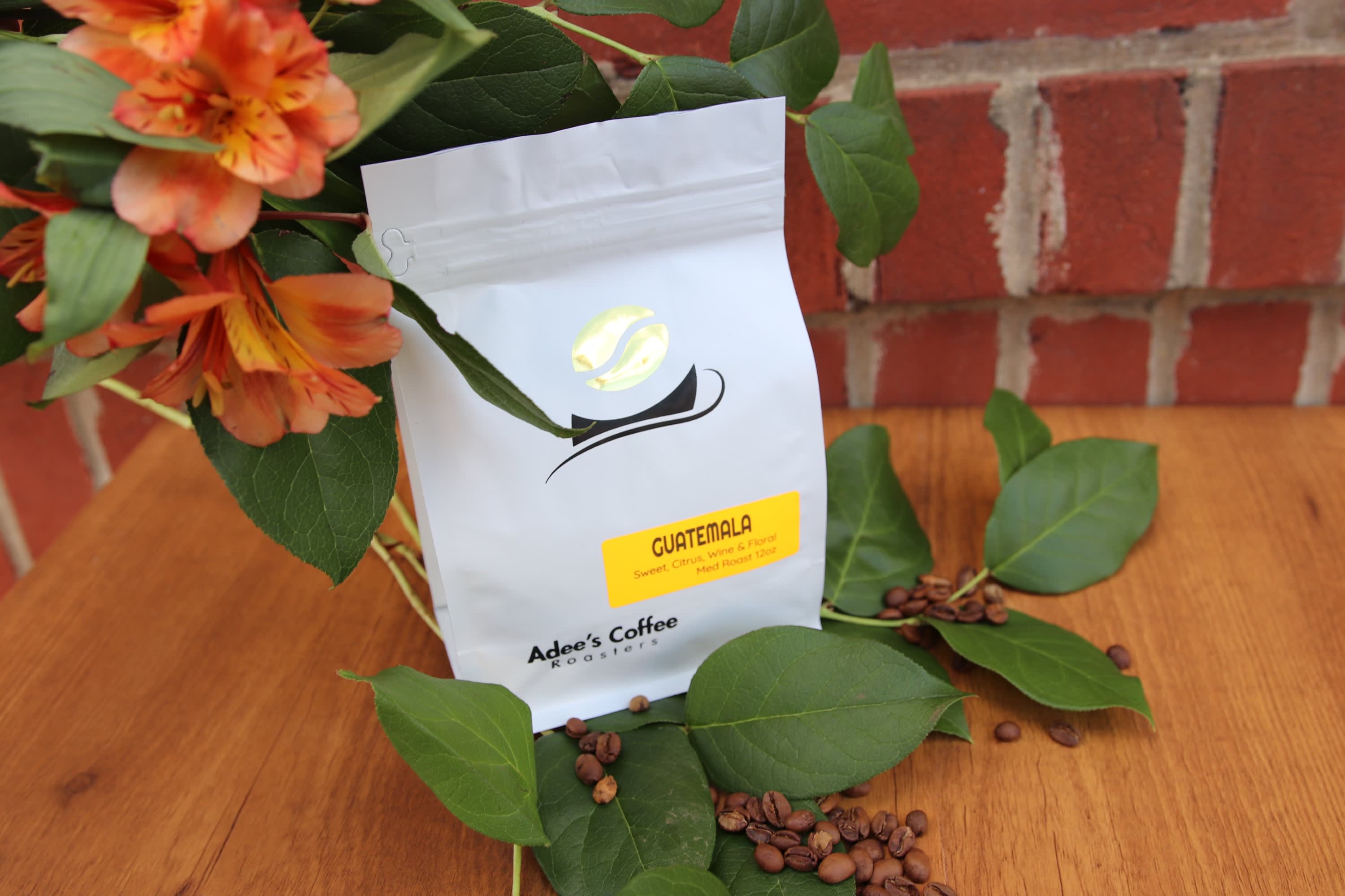 Coffee bag with orange flowers and scattered beans on a wooden surface