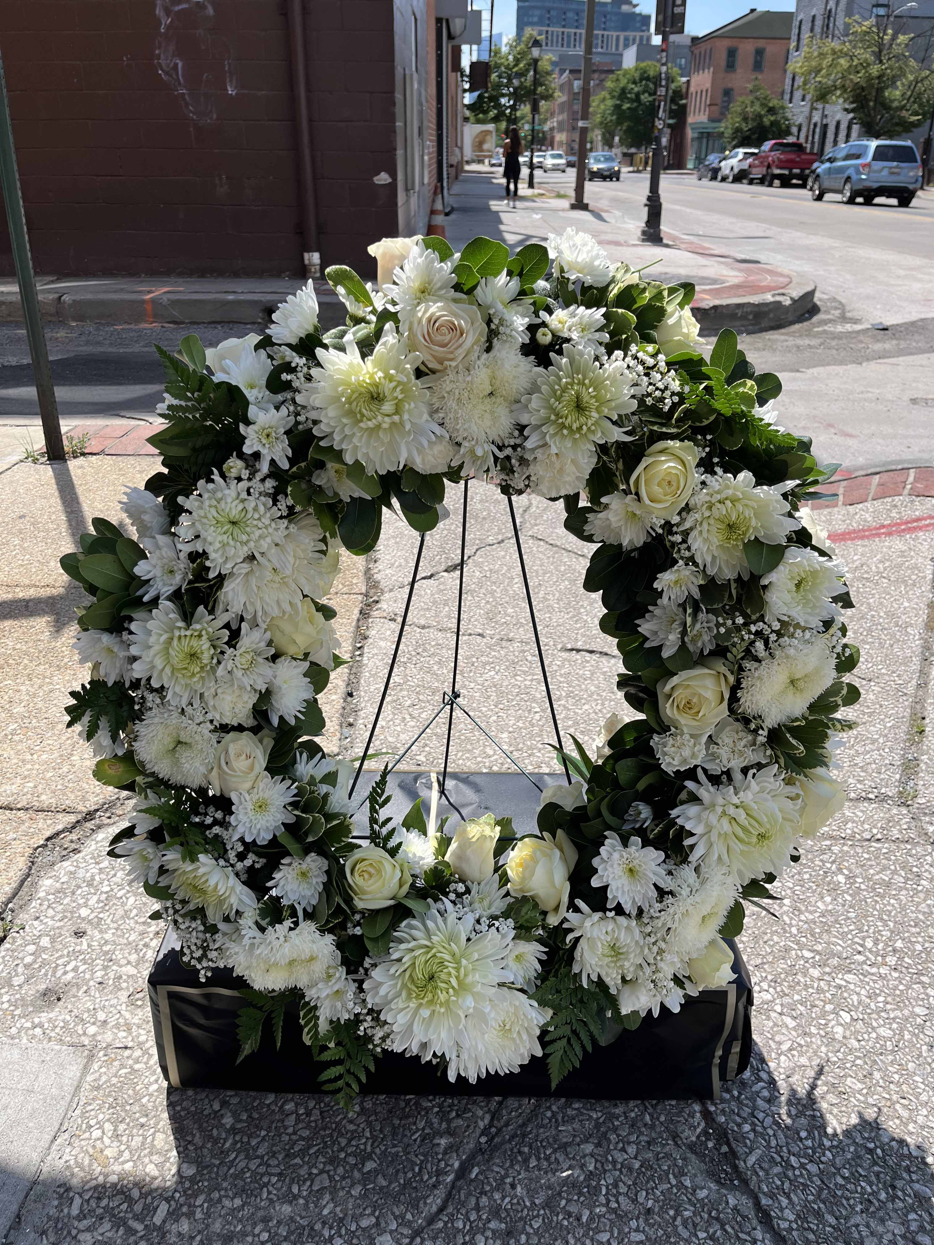 White floral wreath on a stand with roses and daisies