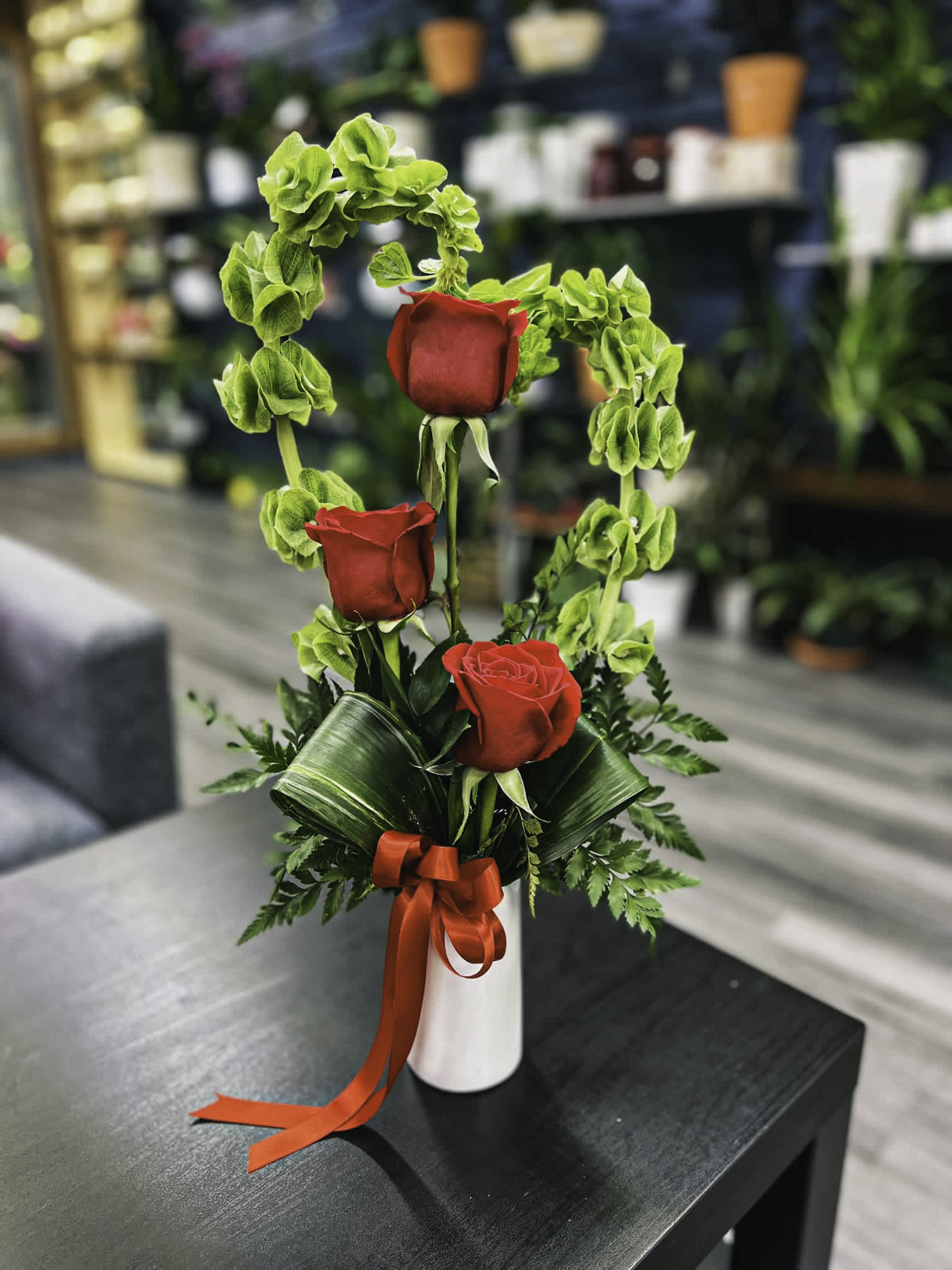 Three red roses with green filler in a white vase tied with a red ribbon