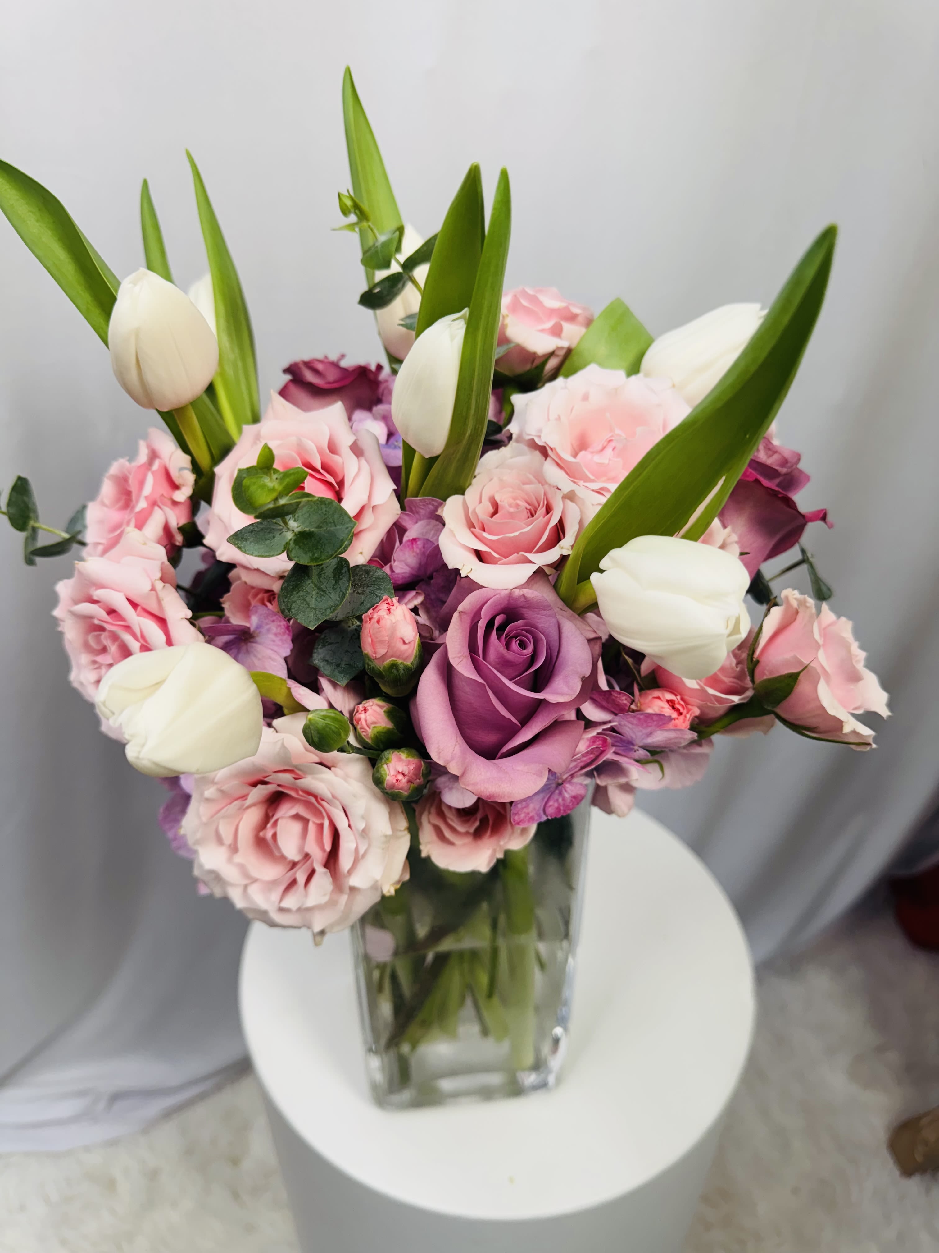 Pink and purple roses with white tulips in a clear glass vase