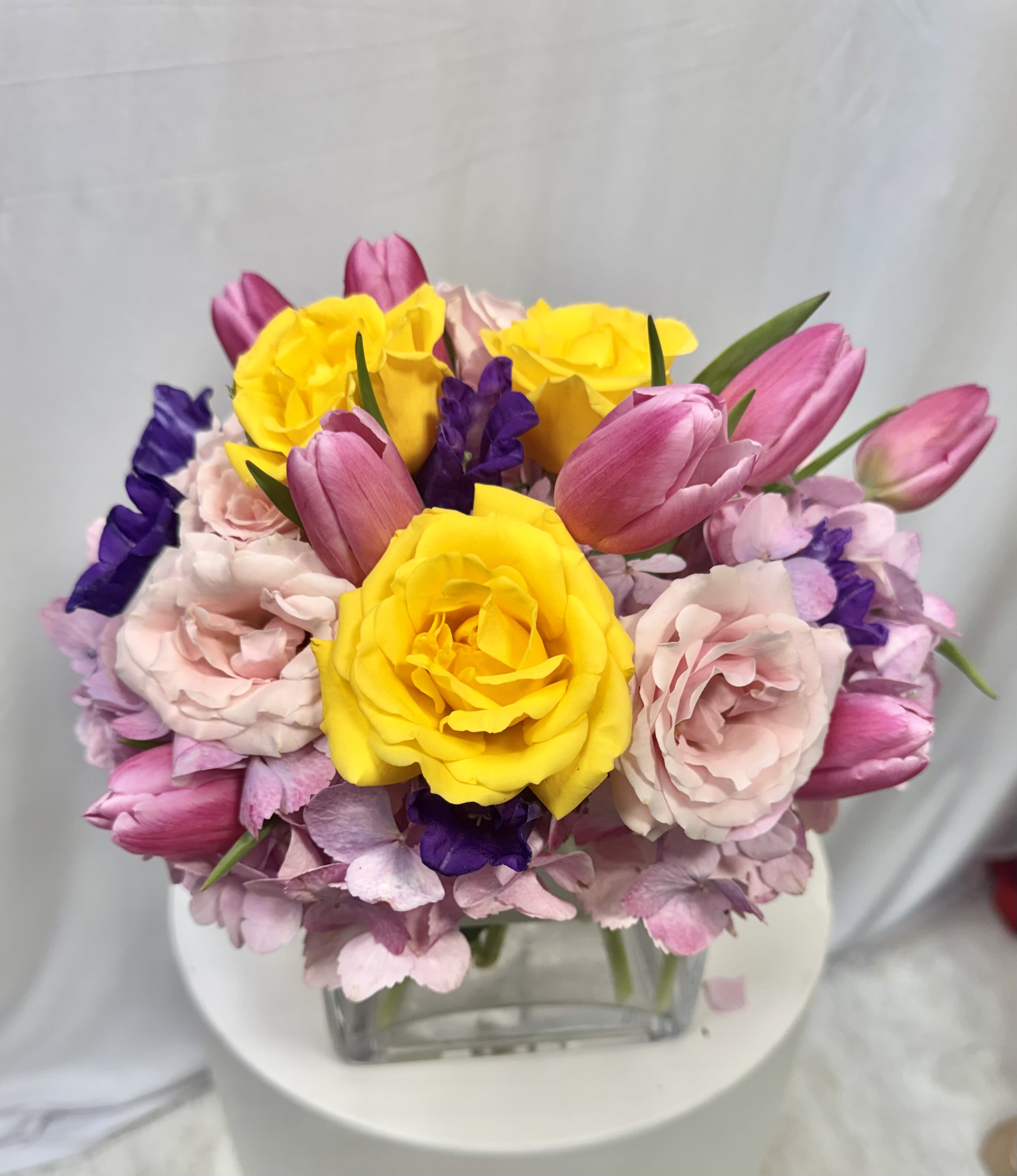 Bouquet of yellow roses, pink tulips, and pale pink flowers in a glass vase