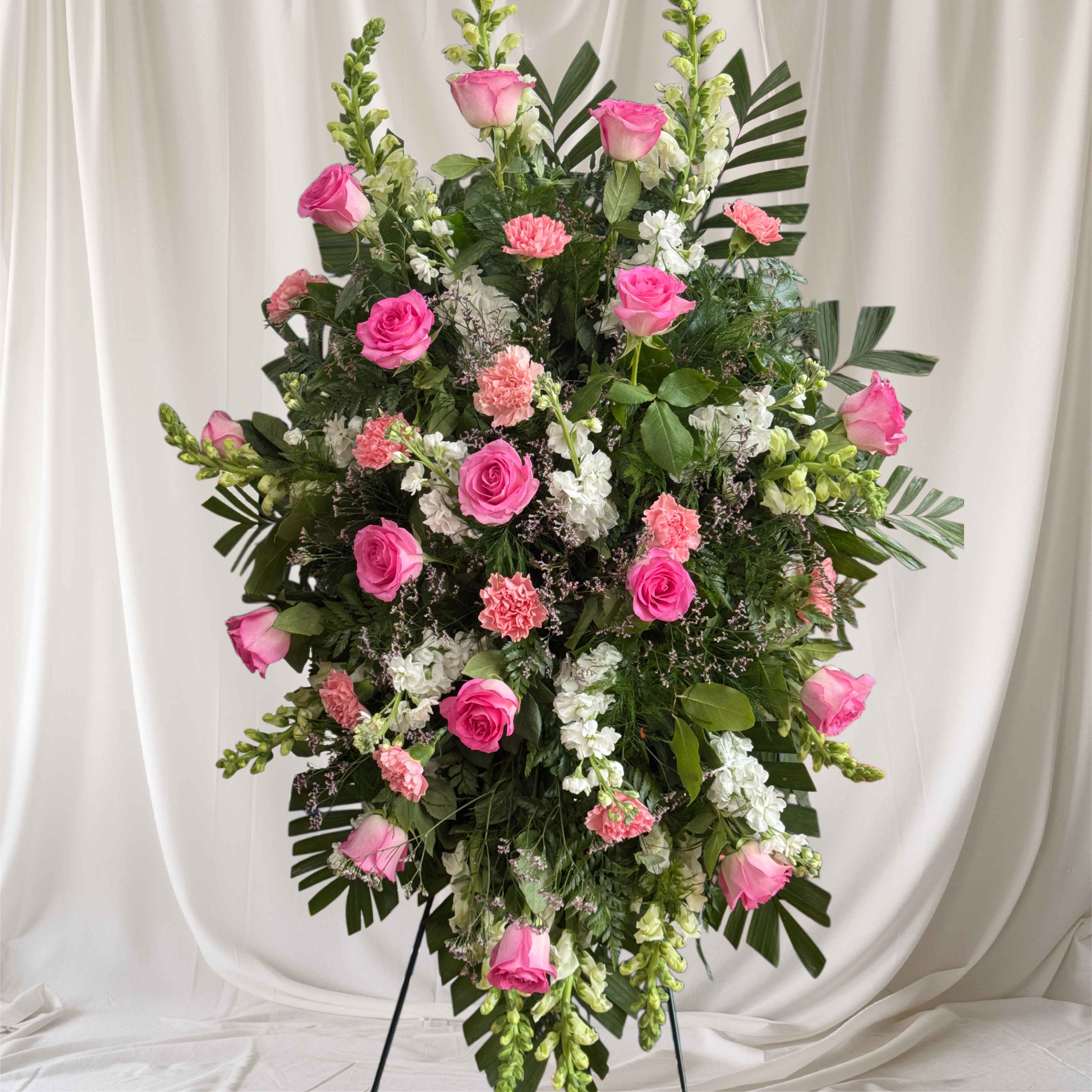 Eternal pink spray stand - Express your deepest condolences with this elegant 52-inch Pink and White Funeral Spray, a graceful tribute designed to honor a beloved life. Arranged on a standing easel, this heartfelt display features a beautiful combination of soft pink and pure white blooms, symbolizing love, remembrance, peace, and admiration. Accented with lush greenery, the arrangement creates a striking yet comforting presentation suitable for funeral services, memorial gatherings, and celebration-of-life ceremonies.  The gentle pink flowers convey affection and gratitude, while the white blooms represent purity, peace, and eternal rest. Carefully handcrafted by skilled florists, this standing spray offers a meaningful expression of sympathy and support during a difficult time.