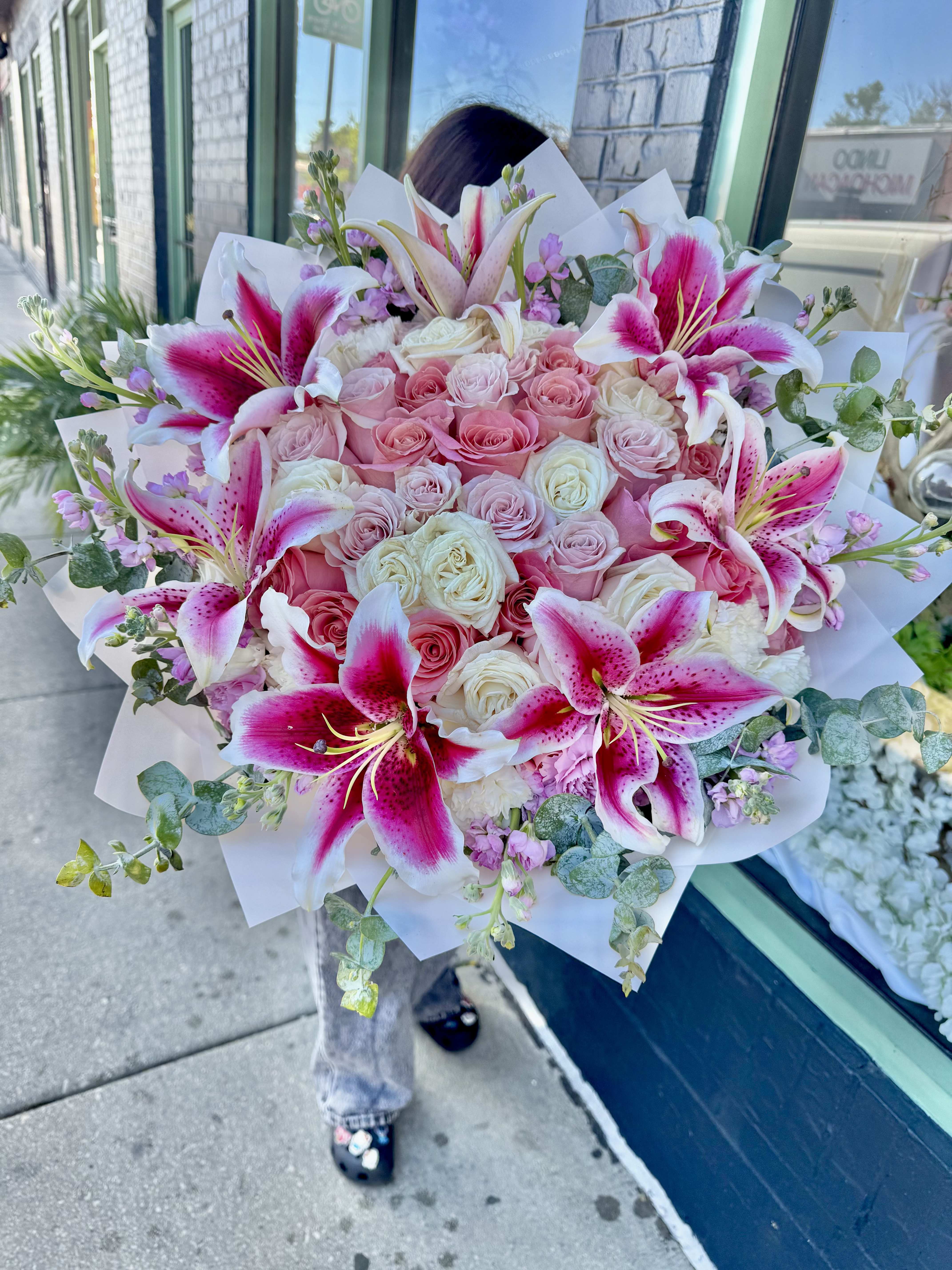 Yours Truly  - Make a grand and unforgettable statement with this luxurious 50-count Pink and White Rose Bouquet. Featuring a stunning blend of premium pink and white roses, this elegant arrangement is beautifully complemented by fragrant stock flowers, graceful lilies, and fresh eucalyptus. The combination of soft pink and crisp white blooms creates a timeless expression of love, admiration, gratitude, and celebration.  Surrounded by lush greenery and expertly wrapped in premium designer paper, this bouquet offers a sophisticated presentation that enhances the beauty of every stem. The delicate fragrance of stock and lilies adds depth and charm, while eucalyptus provides texture and a fresh, natural finish. Perfect for anniversaries, birthdays, congratulations, sympathy gestures, or any occasion that calls for an extraordinary floral gift.