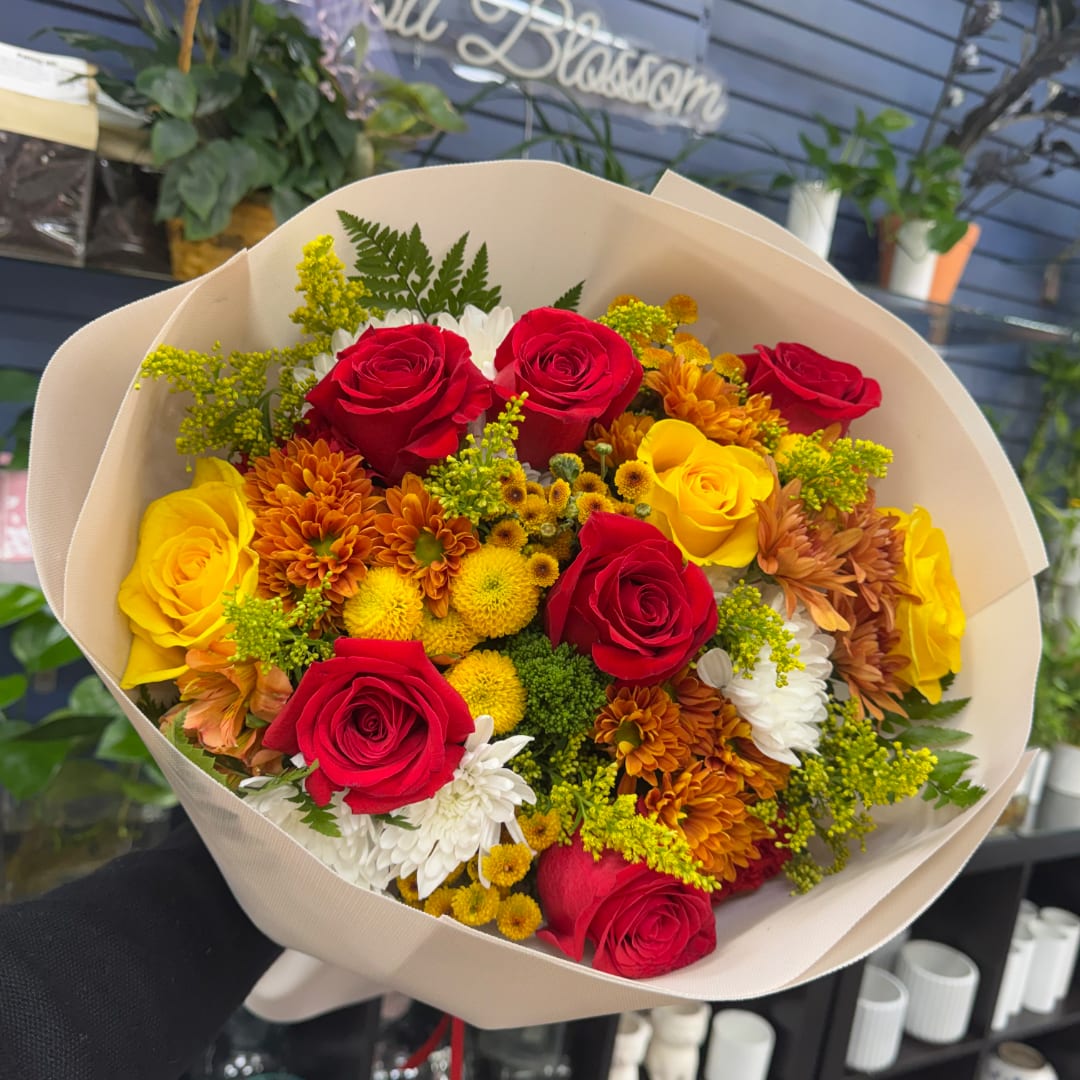 Bouquet of red and yellow roses with orange and white flowers in cream wrapping