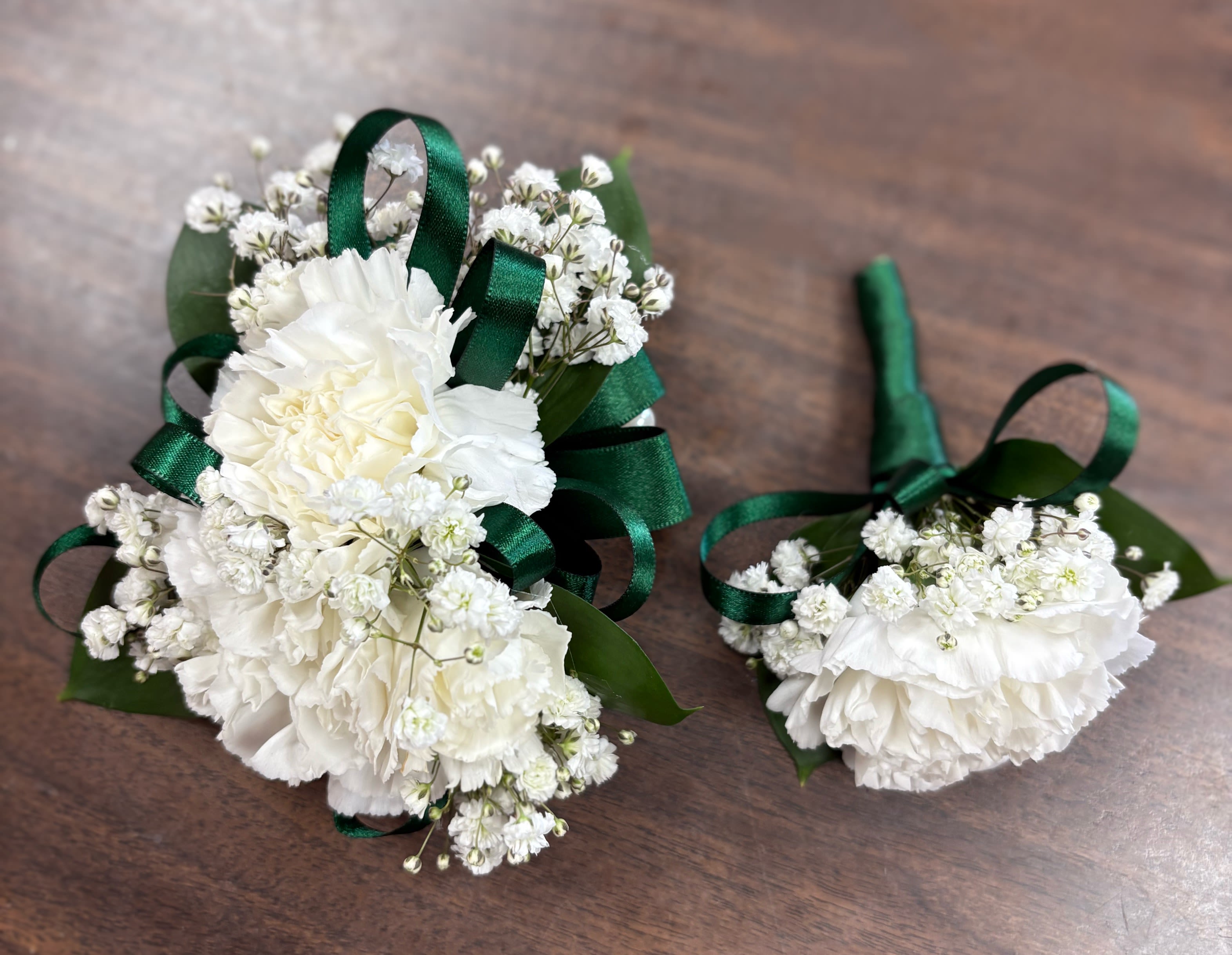 White floral boutonnieres with green ribbon on a wooden surface