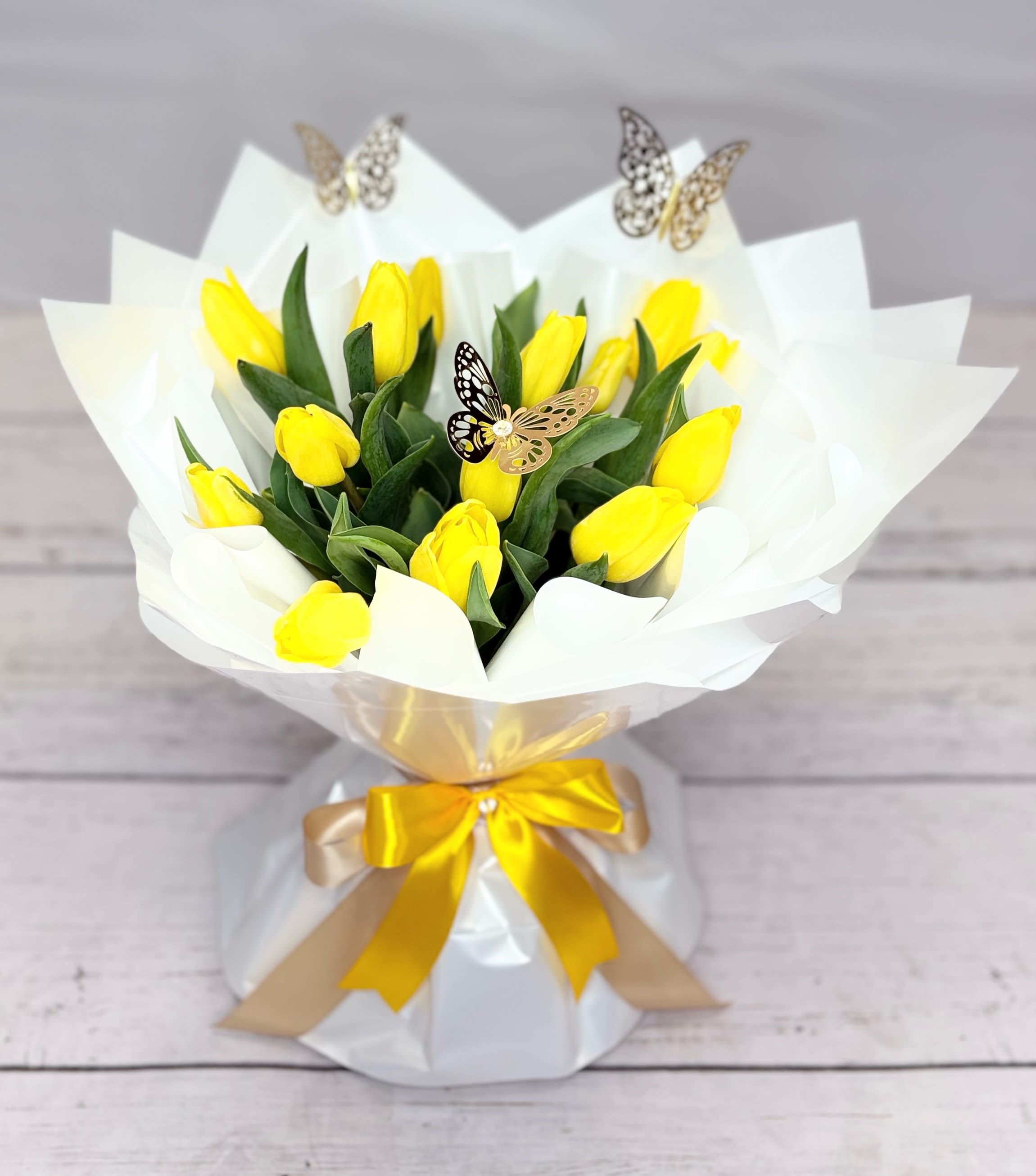 Yellow tulip bouquet wrapped in white paper with a gold ribbon