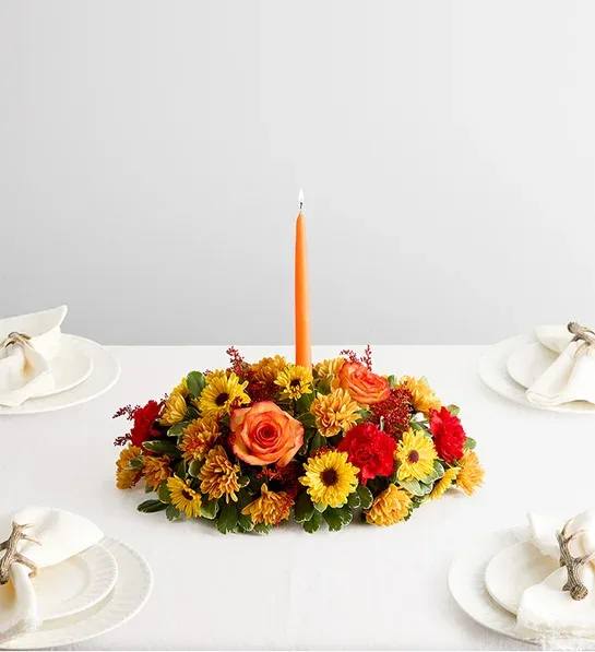 Low floral centerpiece with an orange taper candle