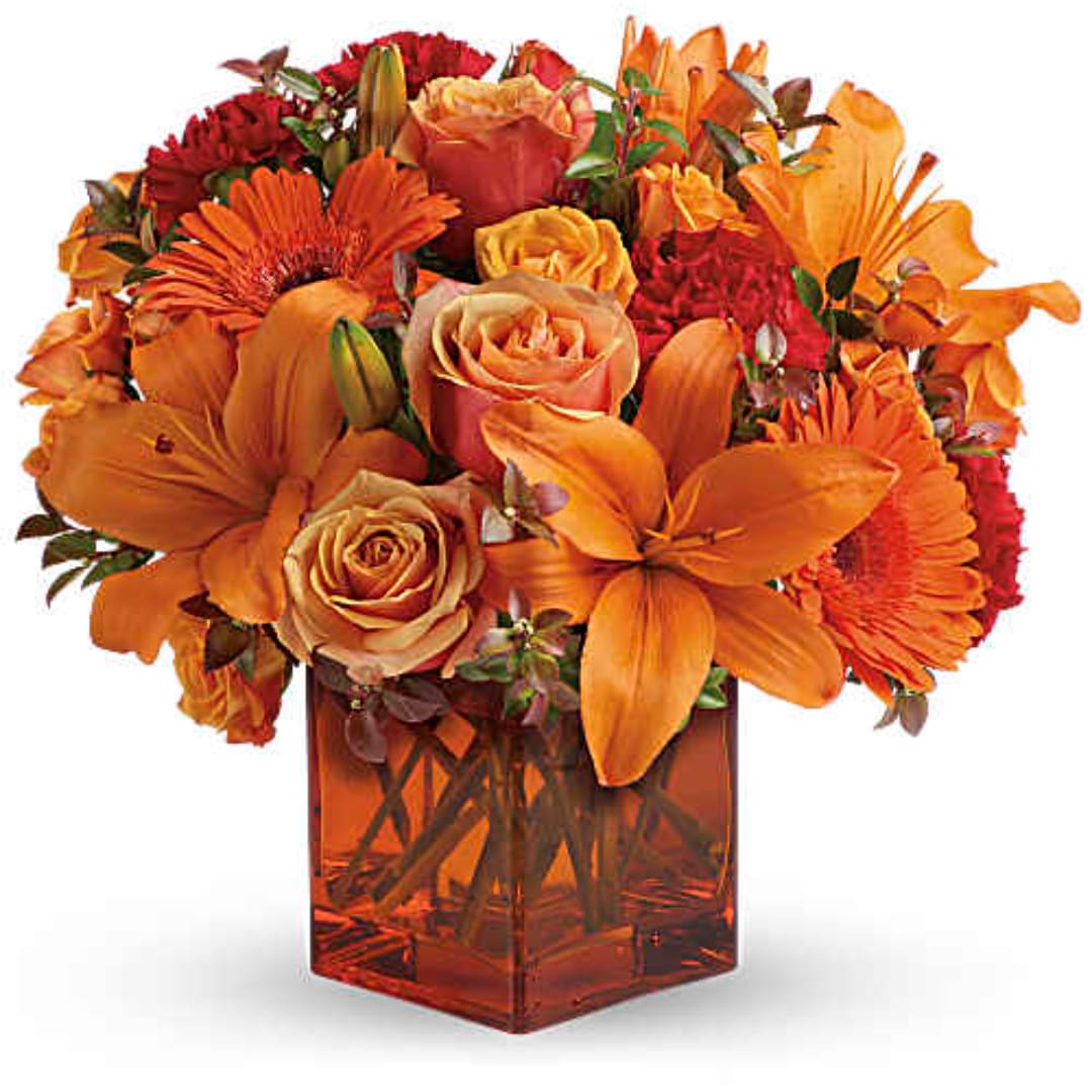 Orange and red mixed bouquet in a square amber vase