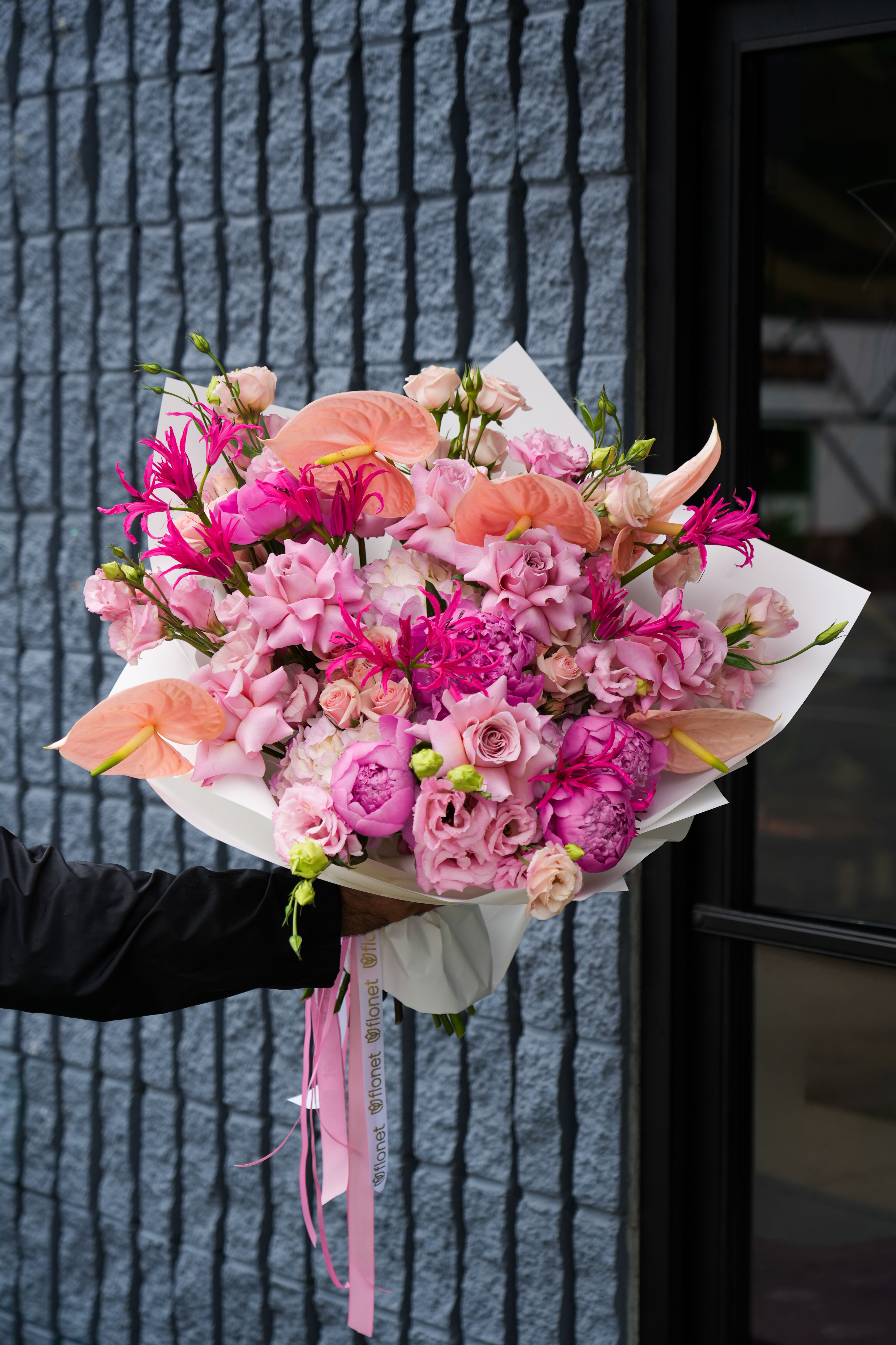 Pink and peach bouquet with anthuriums, roses, and lisianthus wrapped in white paper