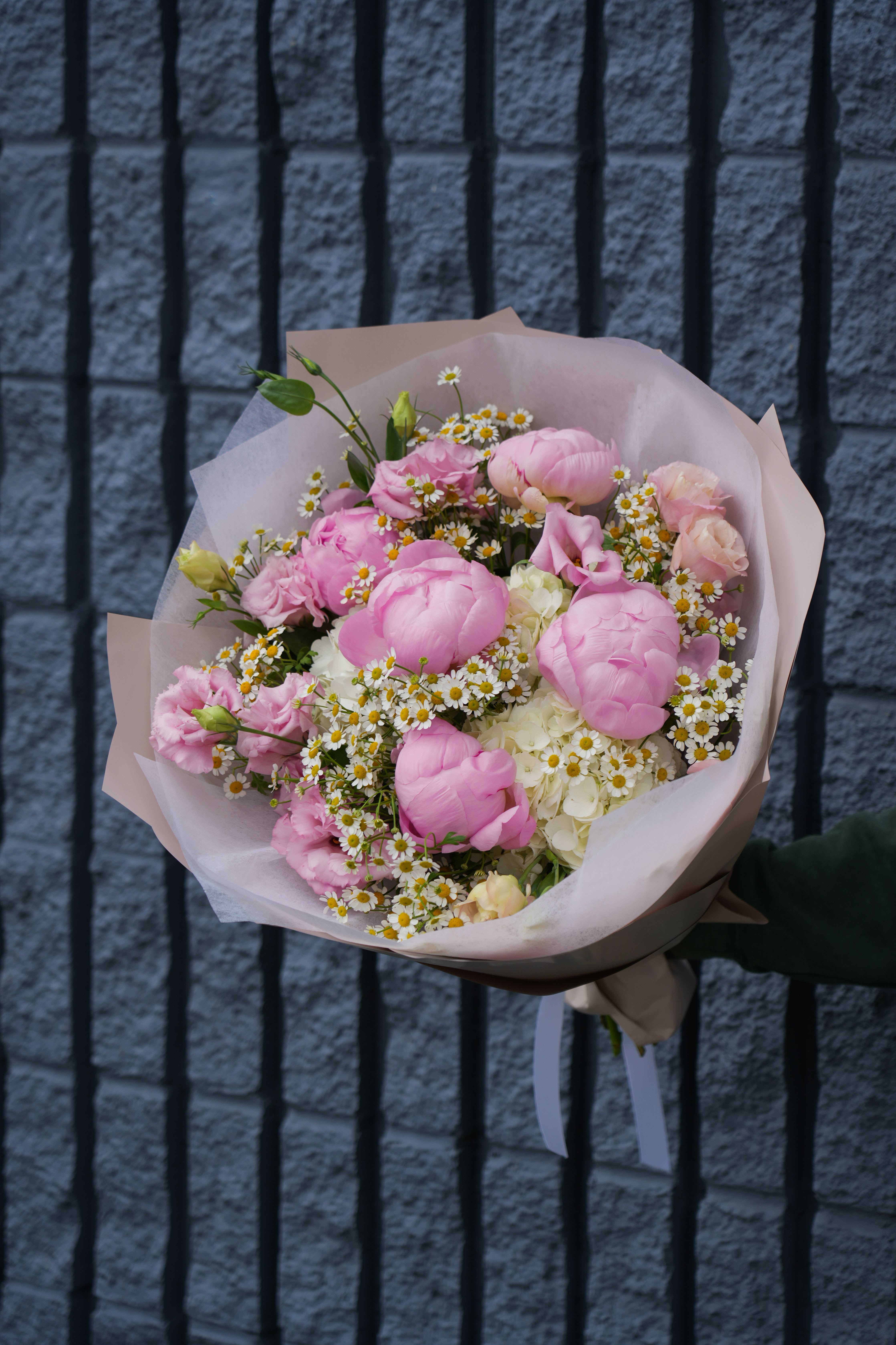 Pink bouquet with white daisy-like flowers wrapped in pale paper