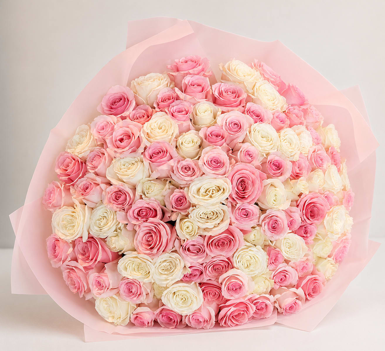 Be Sweet - A lush dome of tightly clustered roses in pink, cream, and peach makes this flower arrangement feel like a soft, timeless embrace - perfect as a birthday bouquet, Mother's Day surprise, anniversary roses, or a "just because" gift. The rounded, full shape reads as romantically feminine without being fussy, so the person you're thinking of will feel cherished the moment they see it.  This large arrangement uses only roses arranged in a dense, domed silhouette so every angle looks abundant and polished. Pale pink paper wrap frames the blooms and reinforces the gentle pastel palette, giving a refined, finished look that's easy to carry and display. The compact, rounded form keeps stems snug and supported for a long-lasting presentation.  Choose this bouquet when you want to make someone feel truly seen and celebrated - a thoughtful, everyday luxury that reads as both intimate and special. Order options include the large, full size shown; standard care is to change the water daily and trim stems for best vase life.