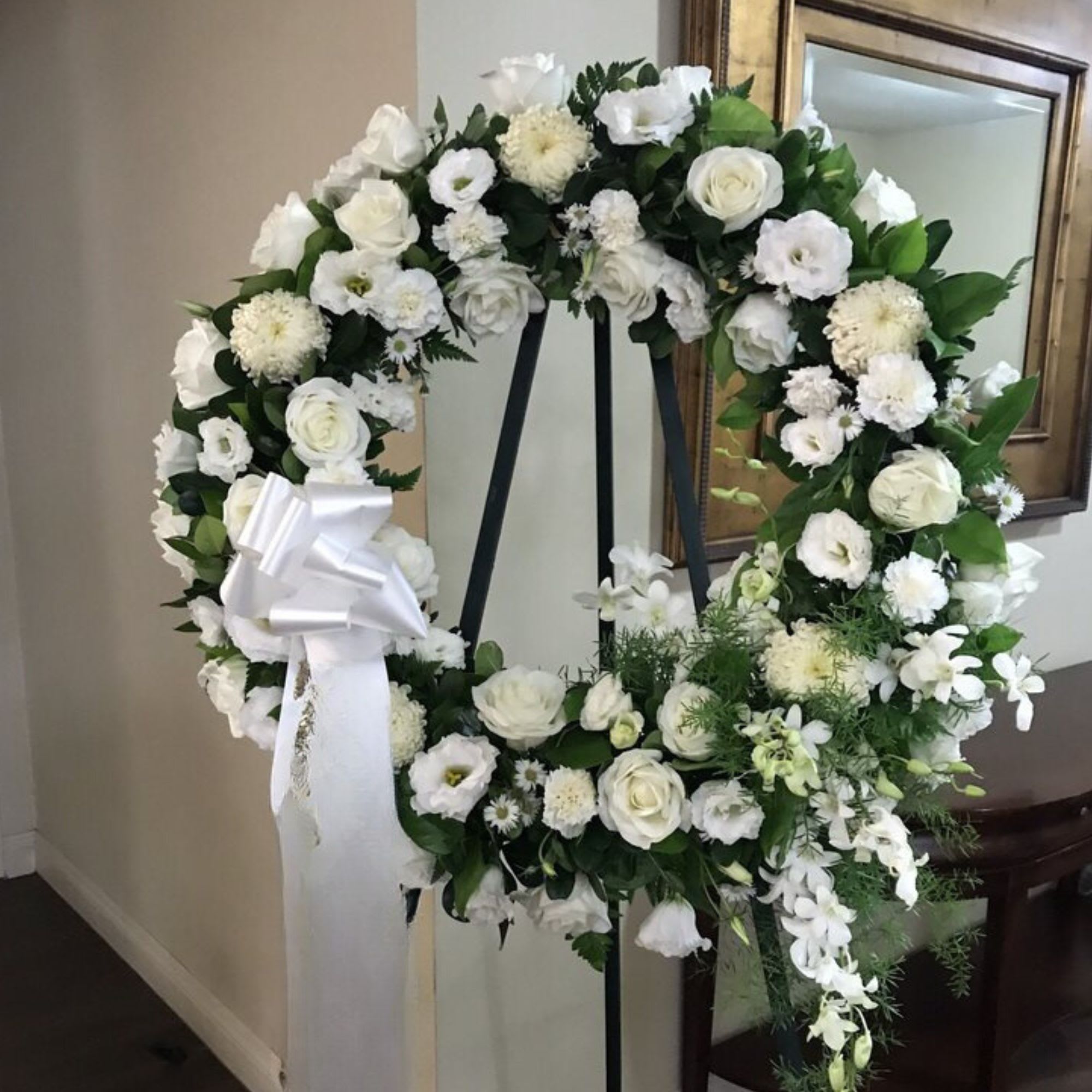 White floral wreath on a black stand with a white ribbon
